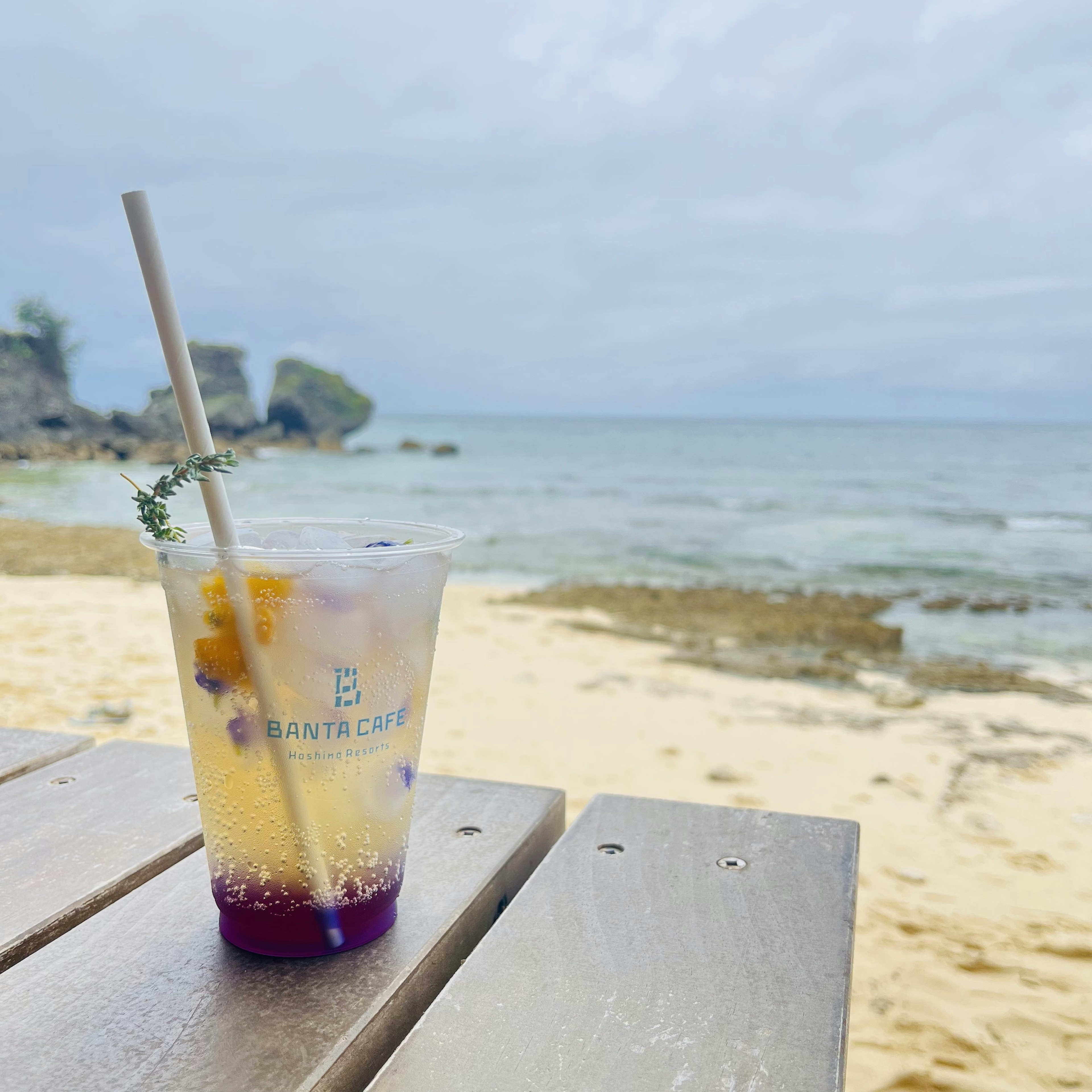 ビーチでのカラフルな飲み物が入ったカップと木製テーブルの風景