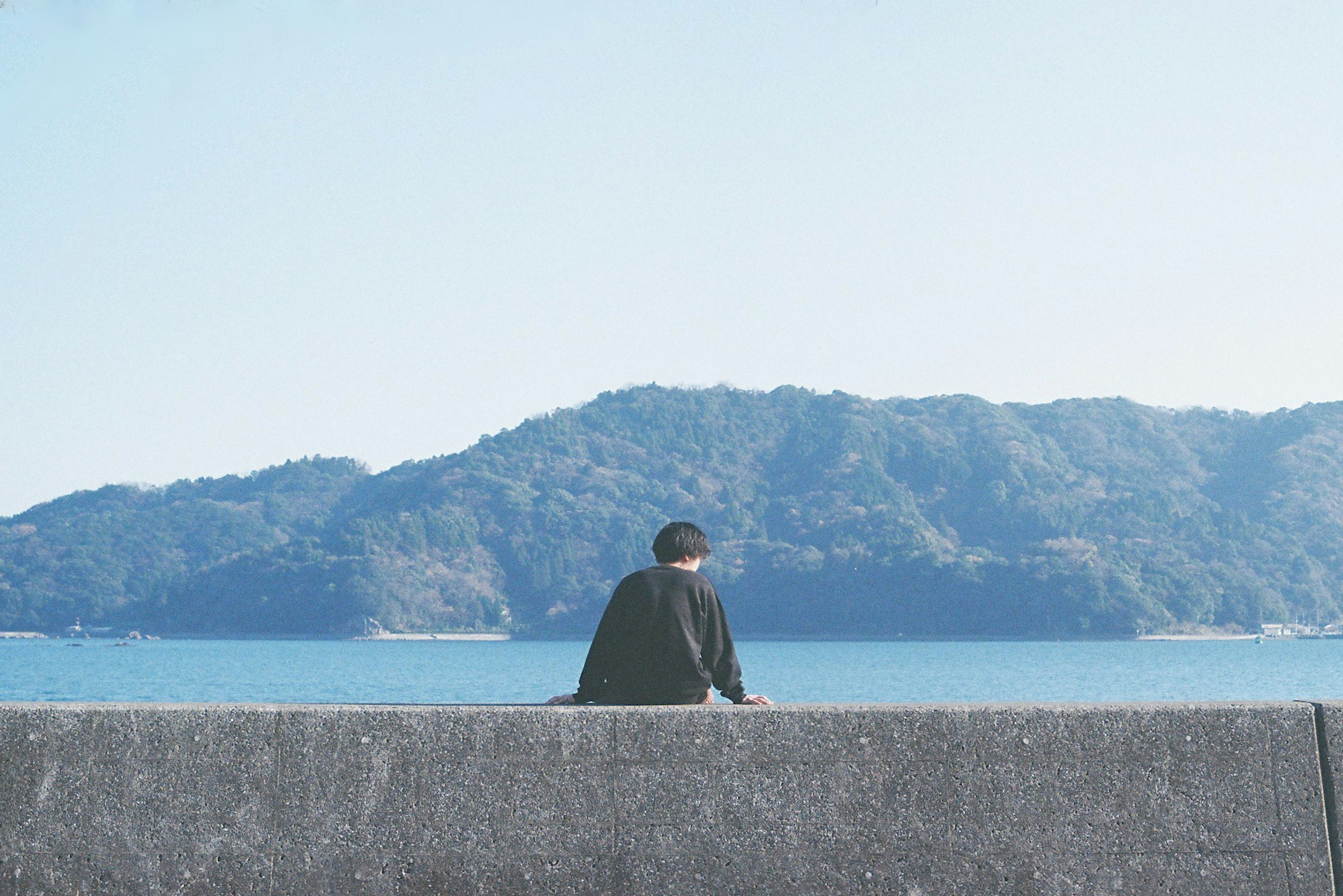 A person sitting with their back towards the viewer overlooking the blue sea and mountains