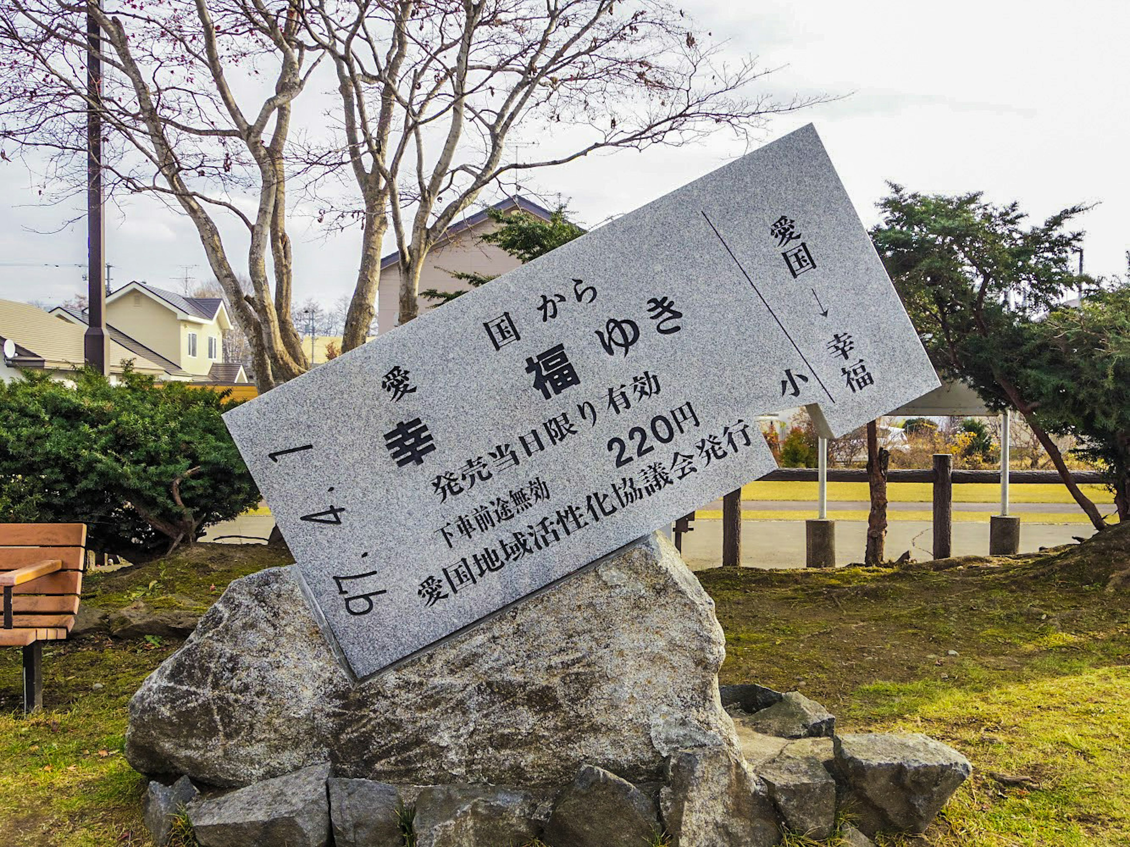 Un cartel montado sobre una piedra rodeado de plantas verdes y casas