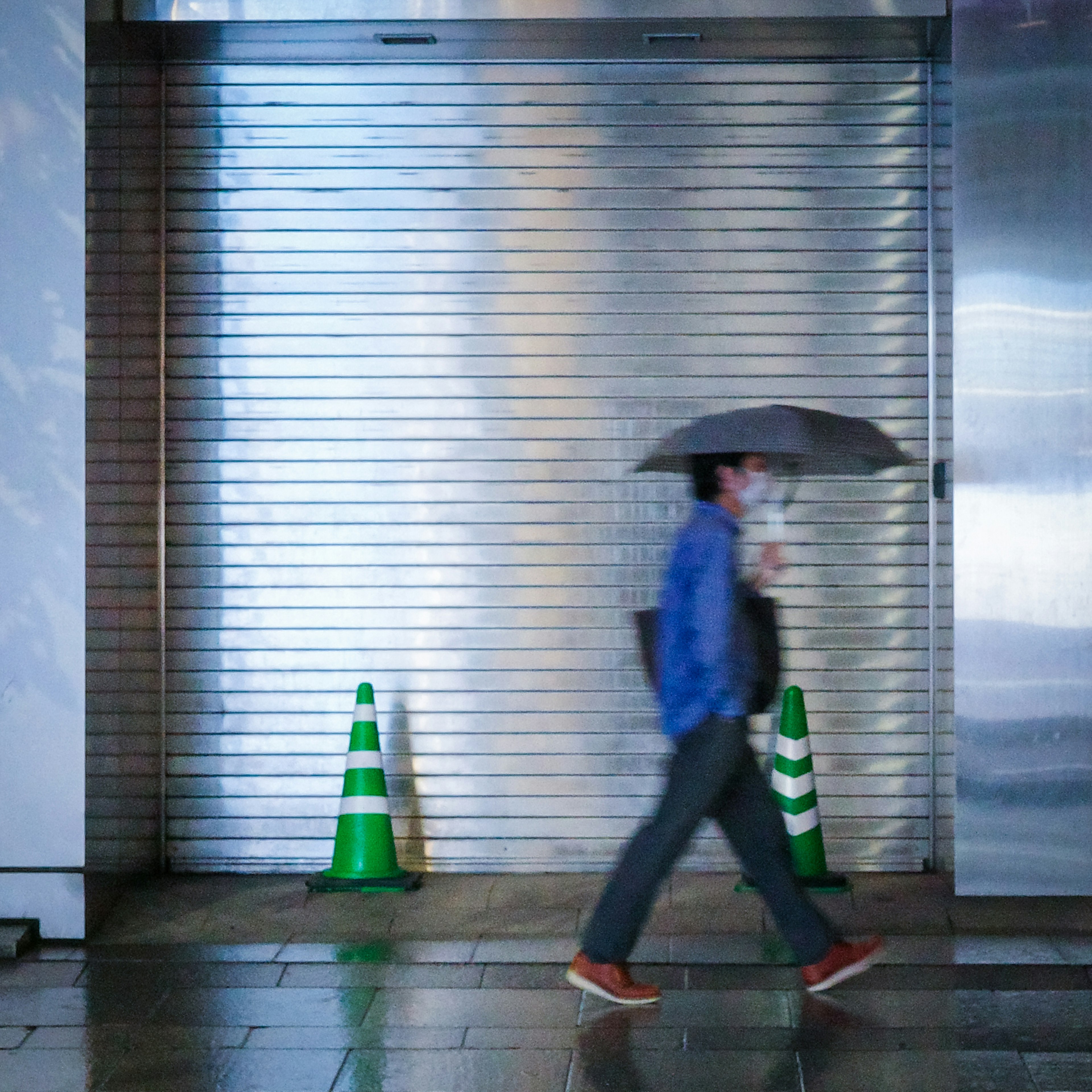 雨の中で傘をさして歩く人と緑のコーンがある街の風景