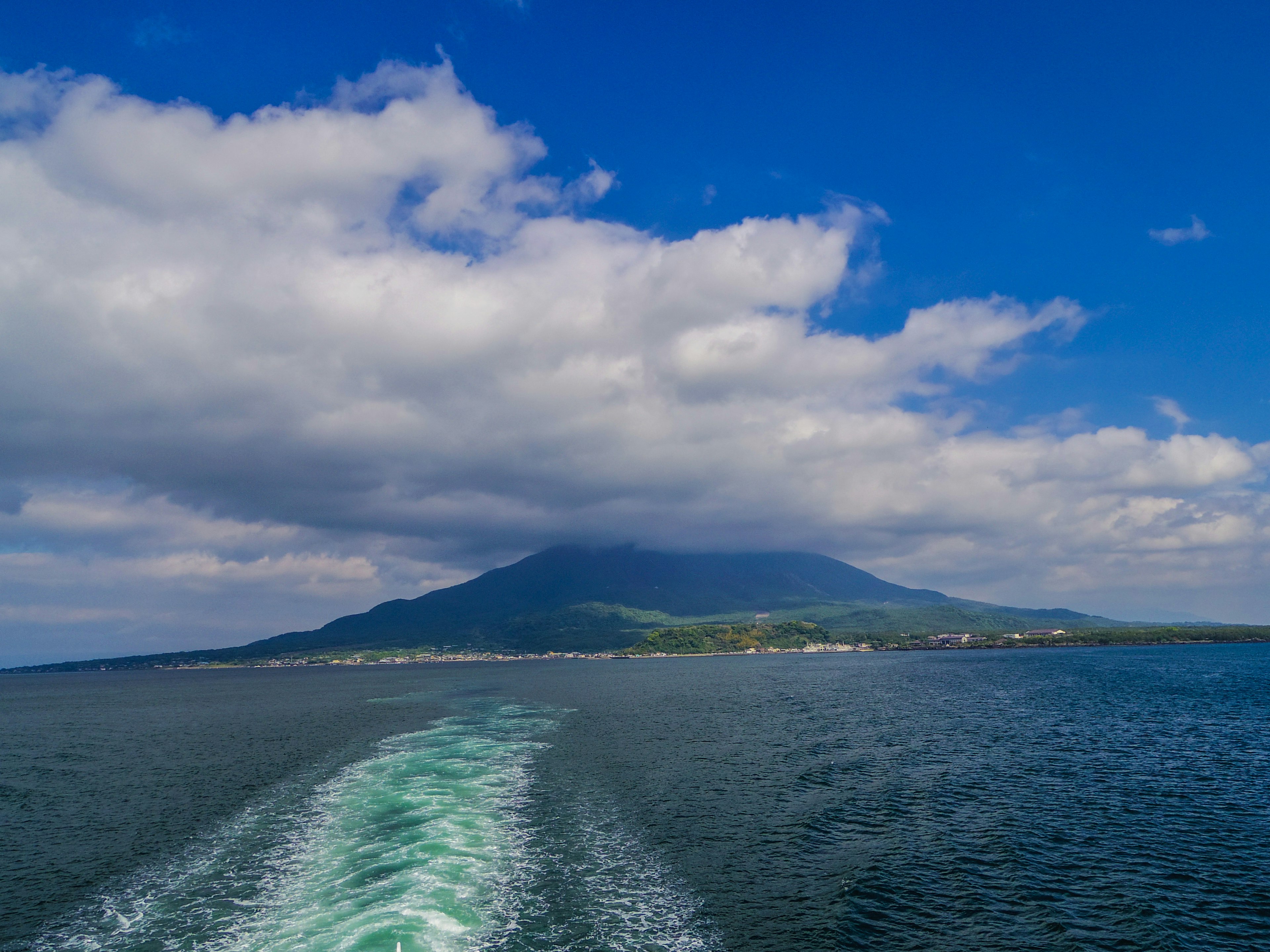 Vista panoramica di una montagna sul mare Cielo azzurro brillante con nuvole Scia di una barca in primo piano