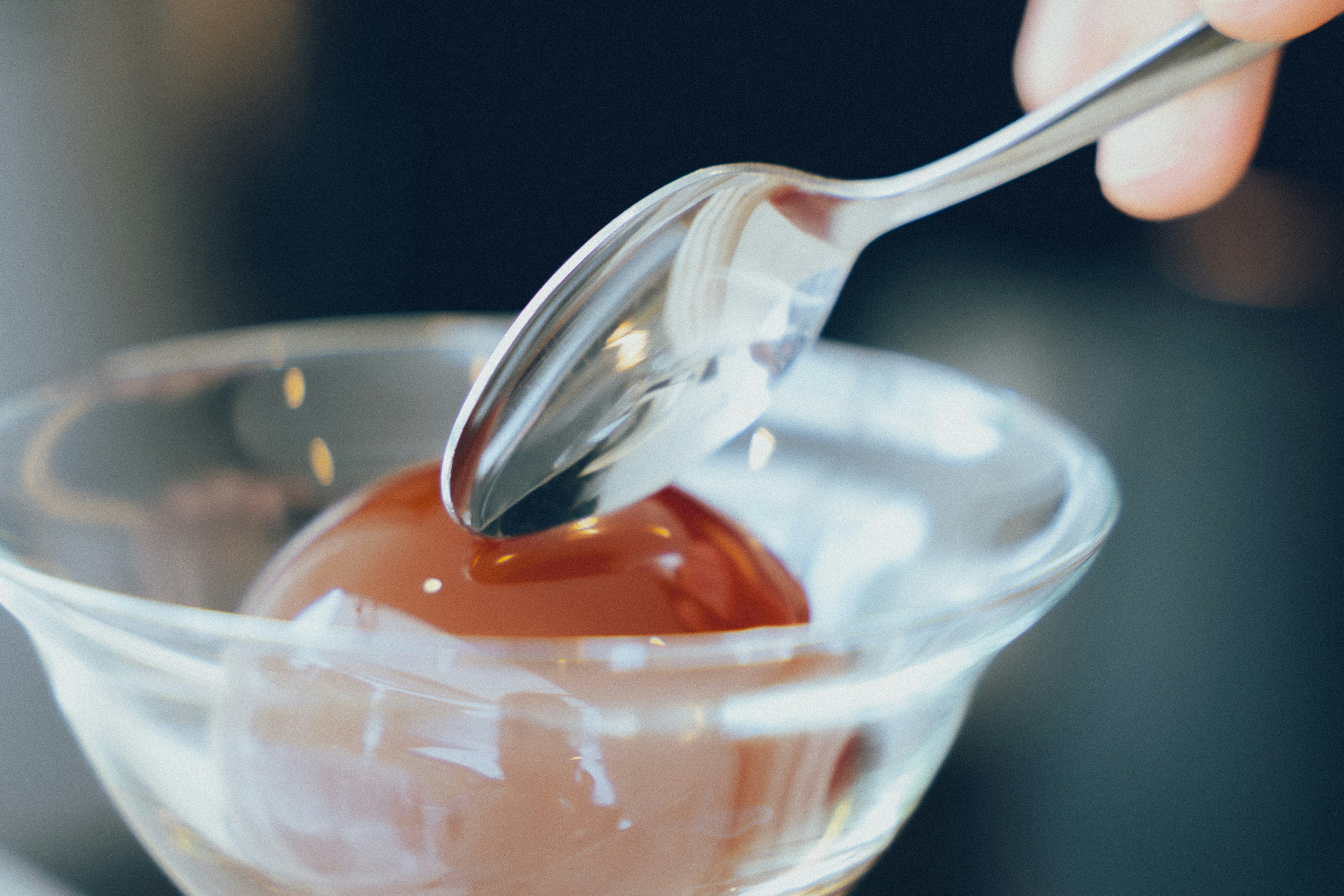 A hand holding a spoon dipping into a chocolate dessert in a clear glass bowl