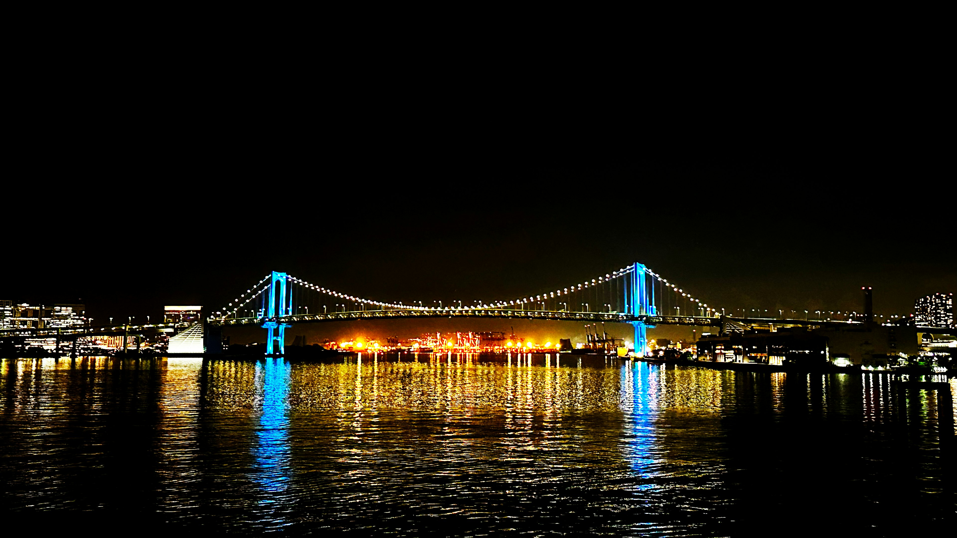 Vista nocturna del Puente Arcoíris iluminado con luces azules sobre el agua