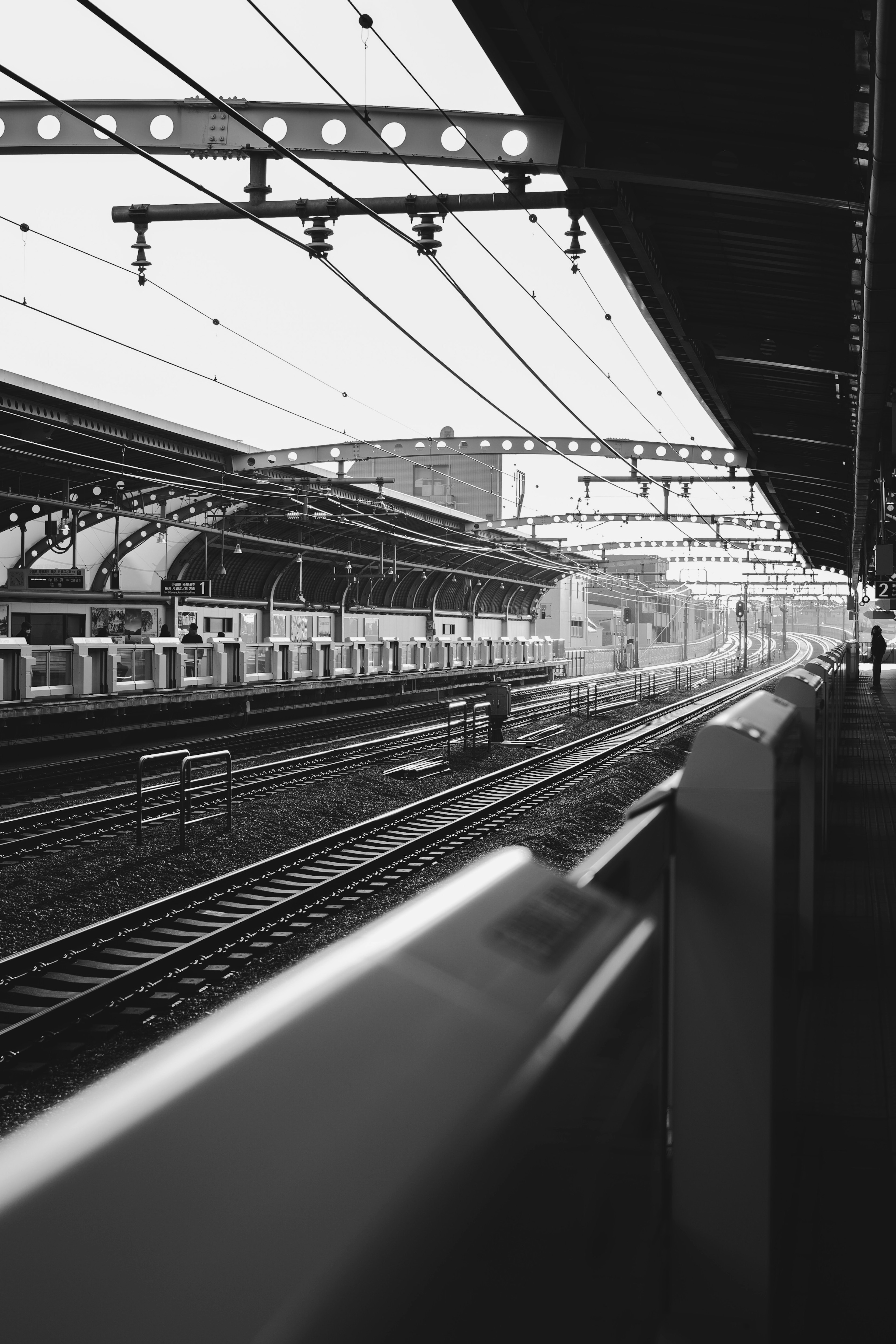 Pemandangan stasiun kereta api hitam putih dengan rel kereta dan struktur di atas