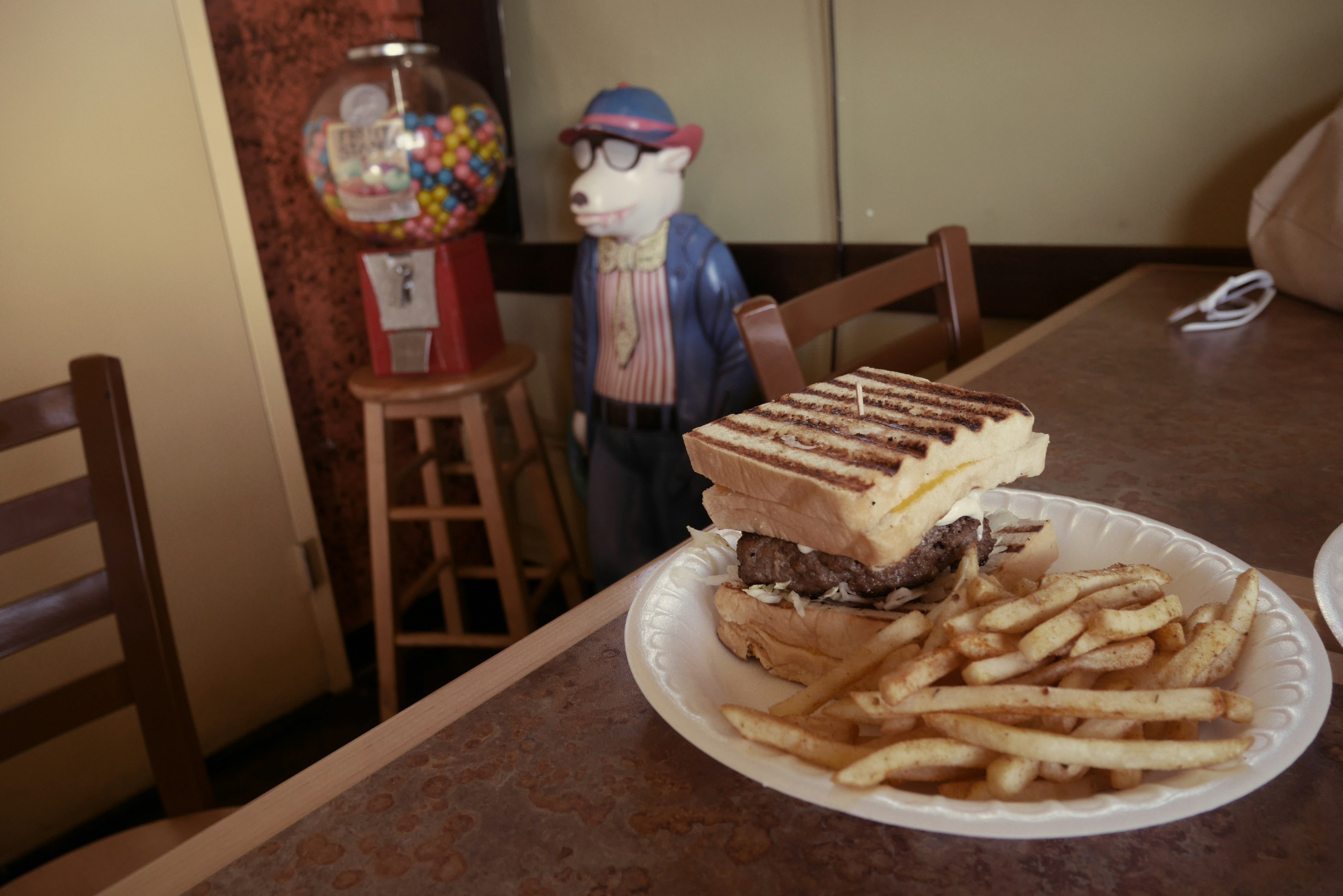 A plate with a sandwich and fries on a table next to a gumball machine and a figurine