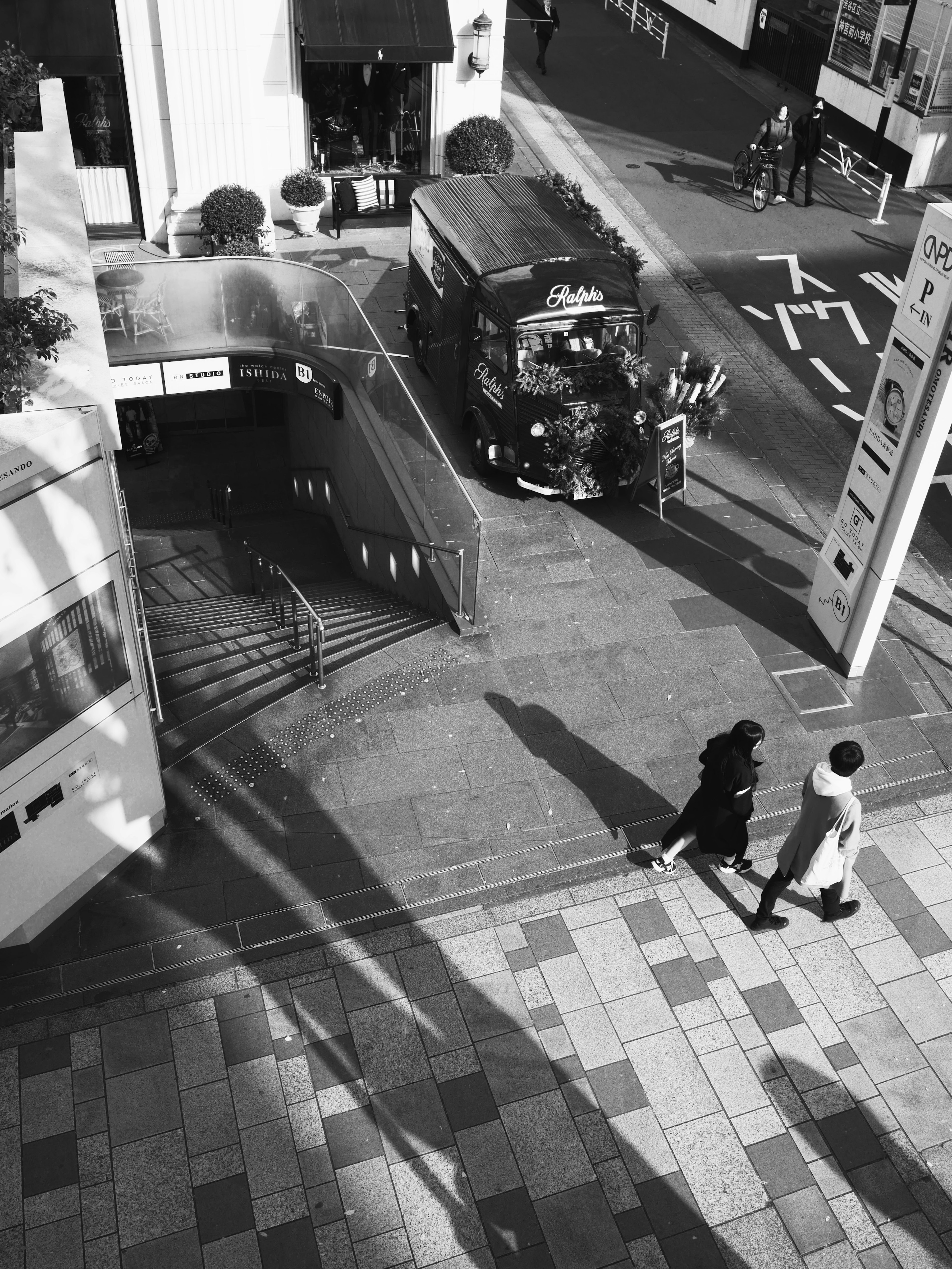 Scène urbaine en noir et blanc avec des personnes marchant entrée de métro visible et bus