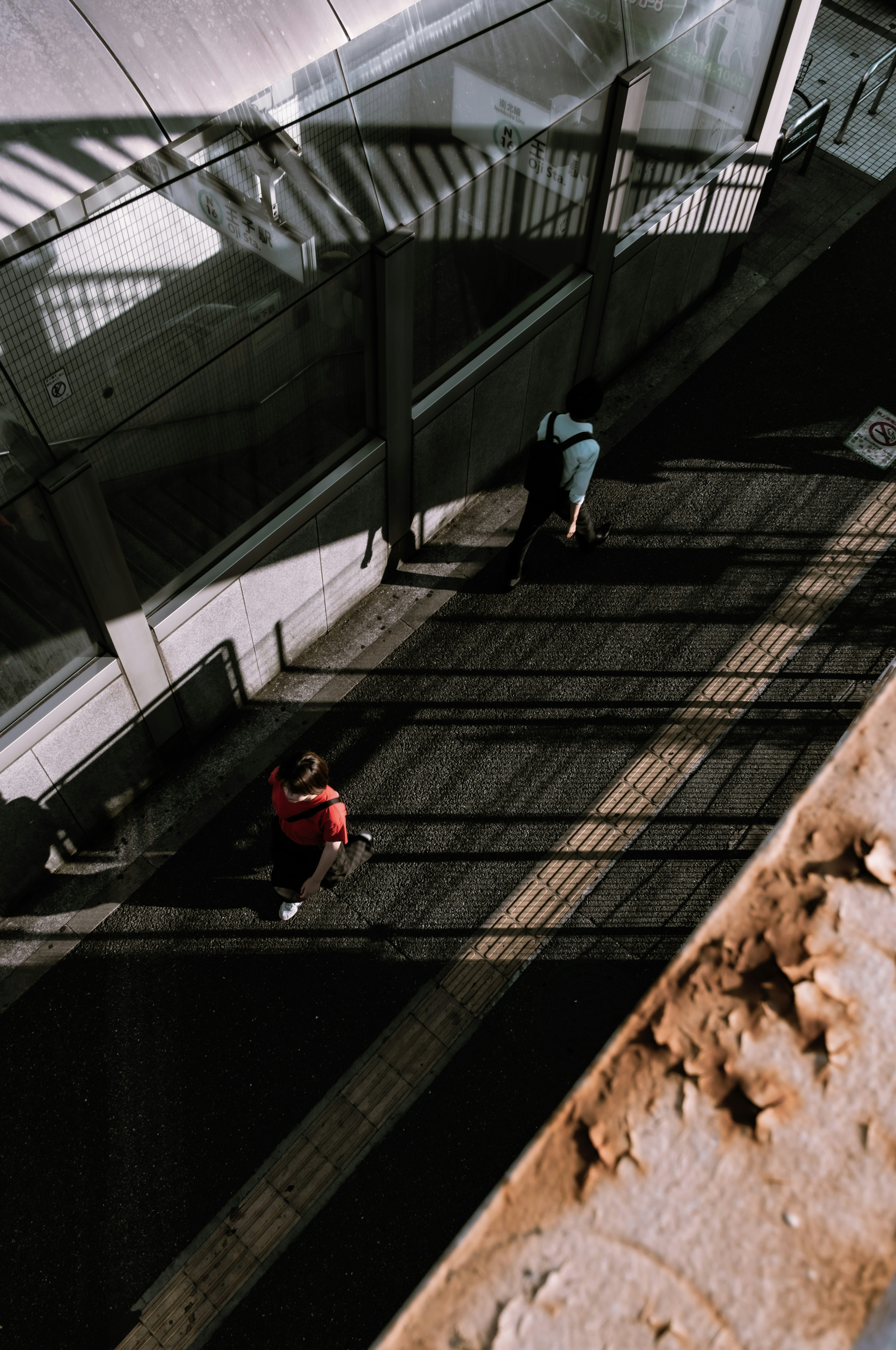 Vista aérea de personas caminando en una estación elevada con contrastes de luz y sombra impresionantes