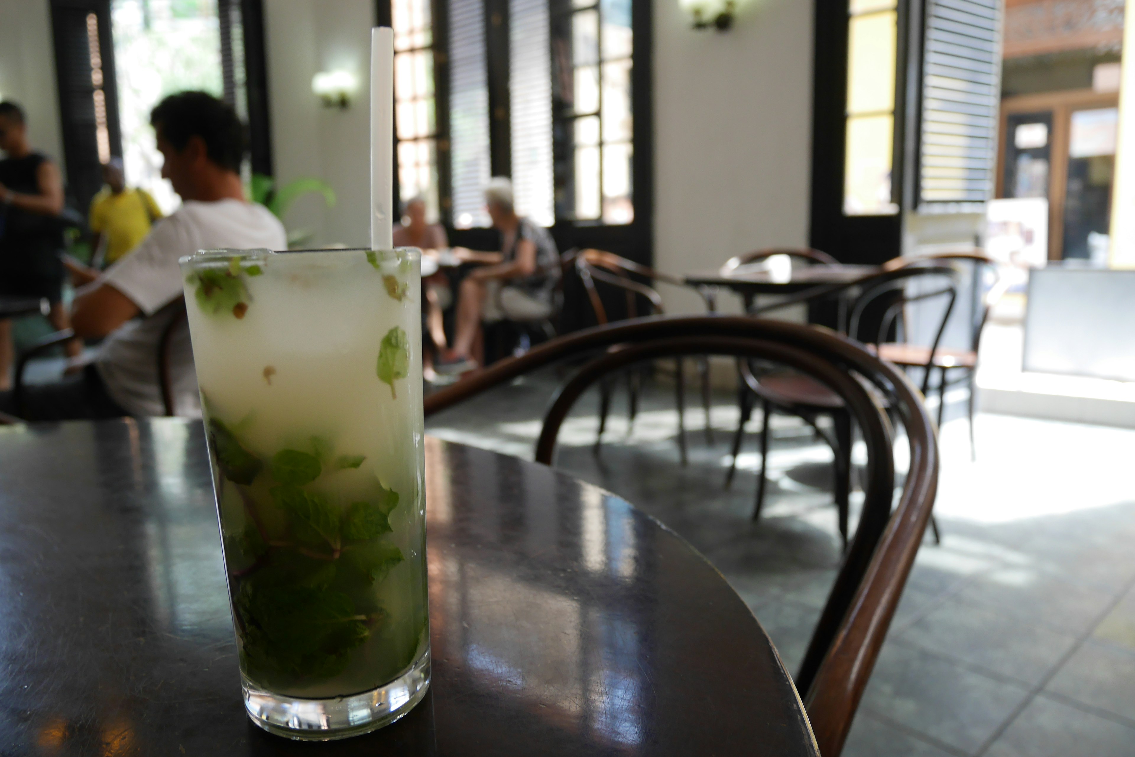 A mojito-style drink with green herbs on a table in a cafe setting