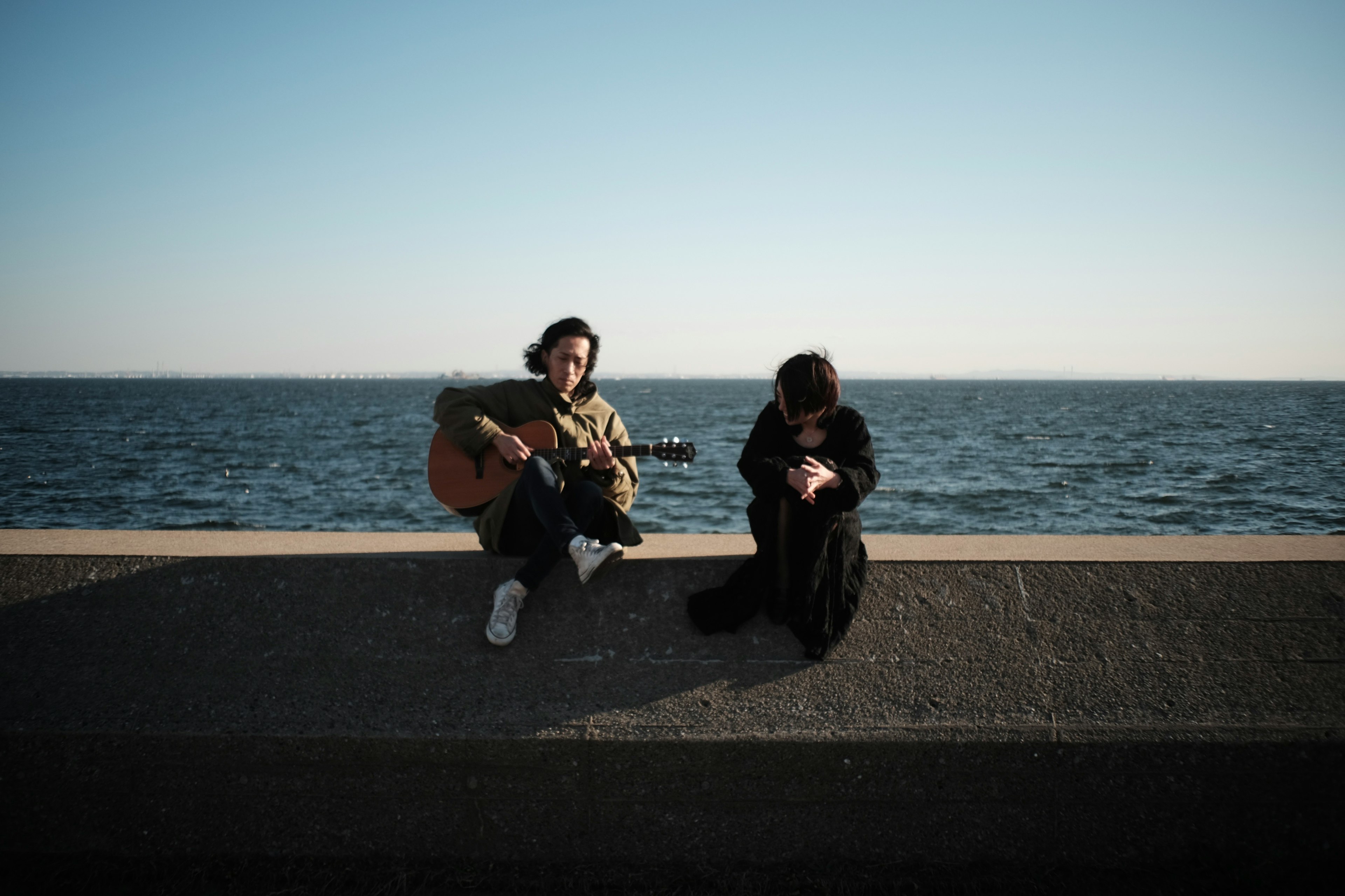 Mann, der am Meer Gitarre spielt, und Frau, die ein Smartphone benutzt