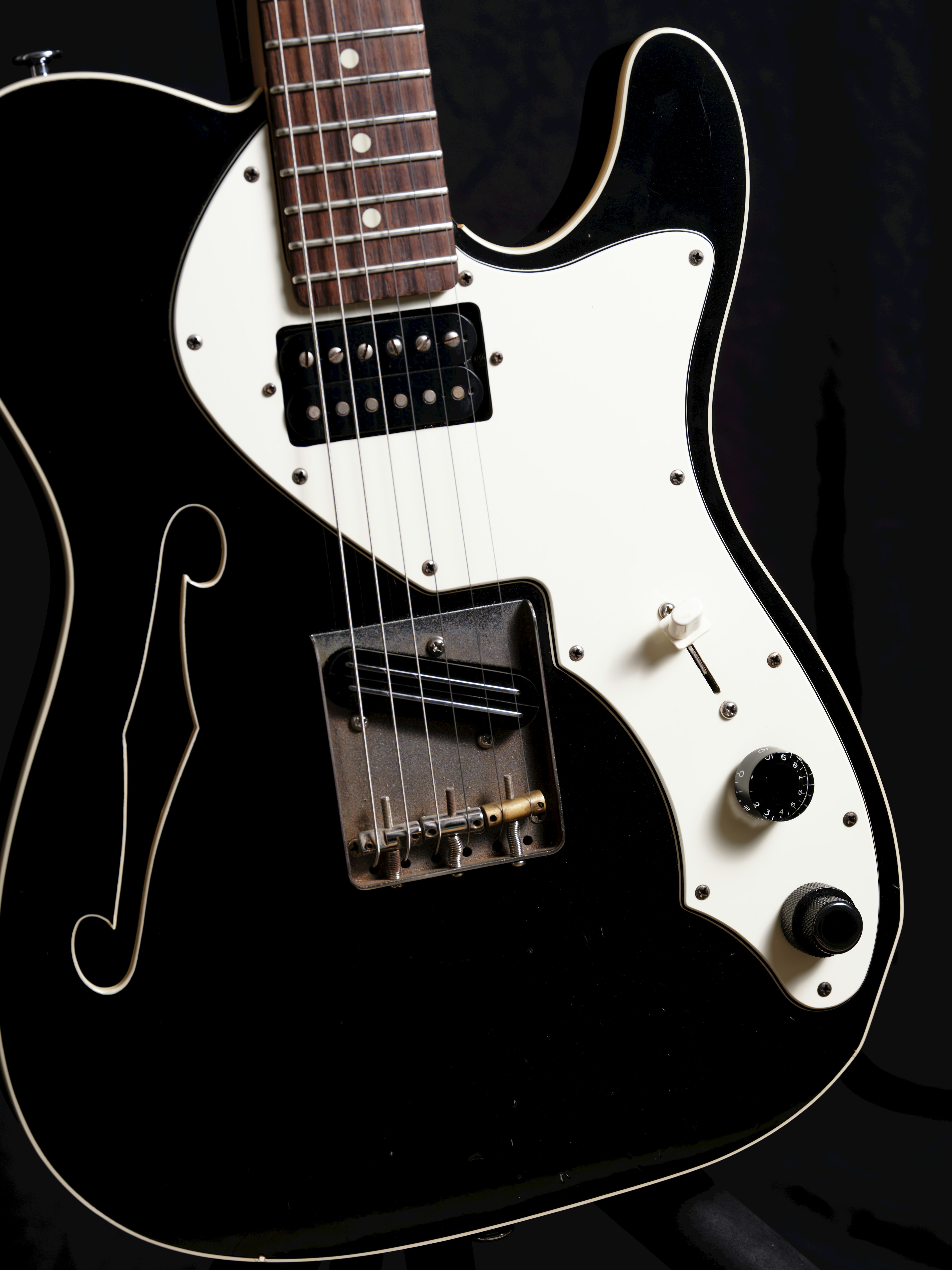 Close-up of a black electric guitar featuring a white pickguard and metallic parts