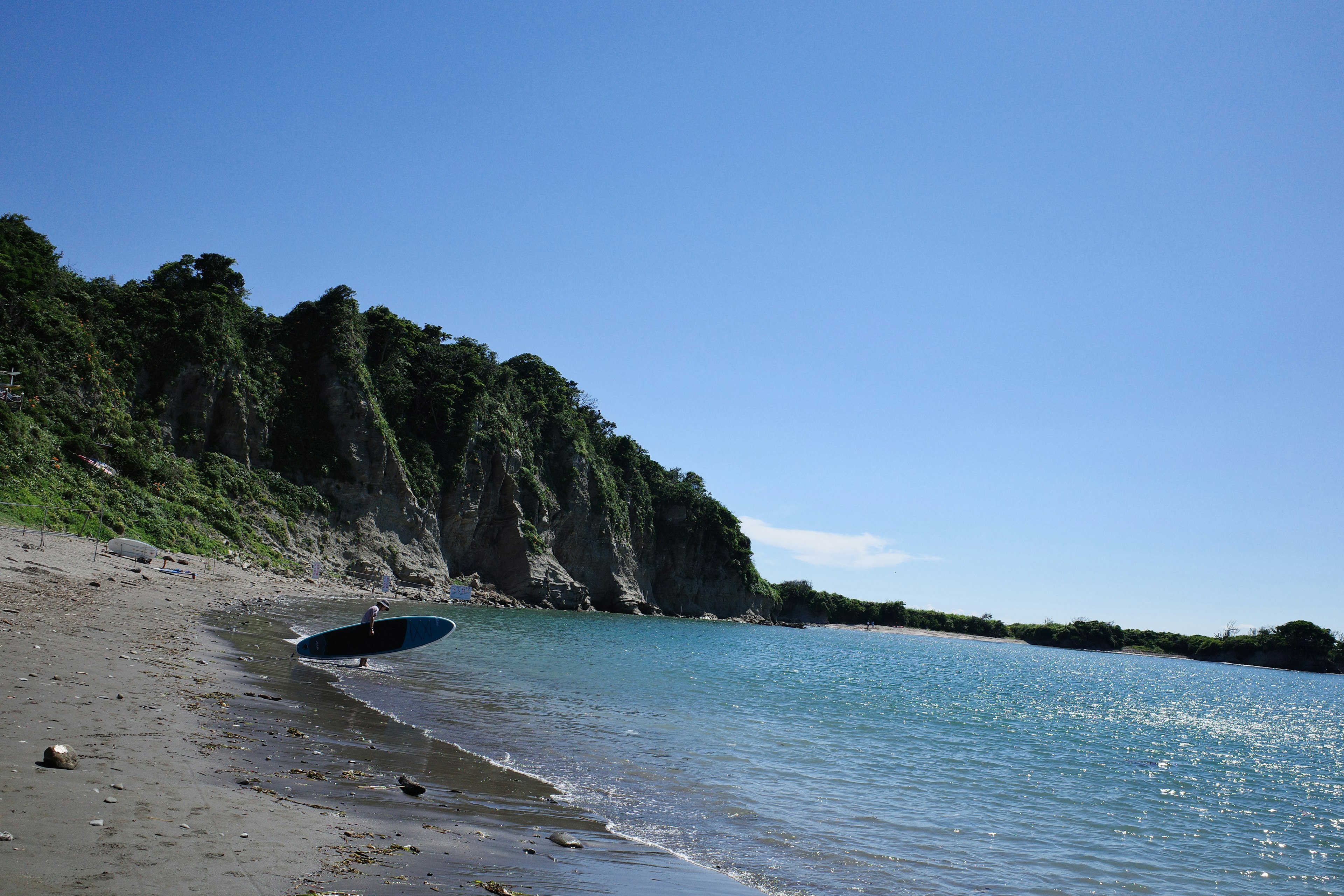 Strandszene mit blauem Himmel und ruhigem Meer mit einem Boot und grünen Klippen