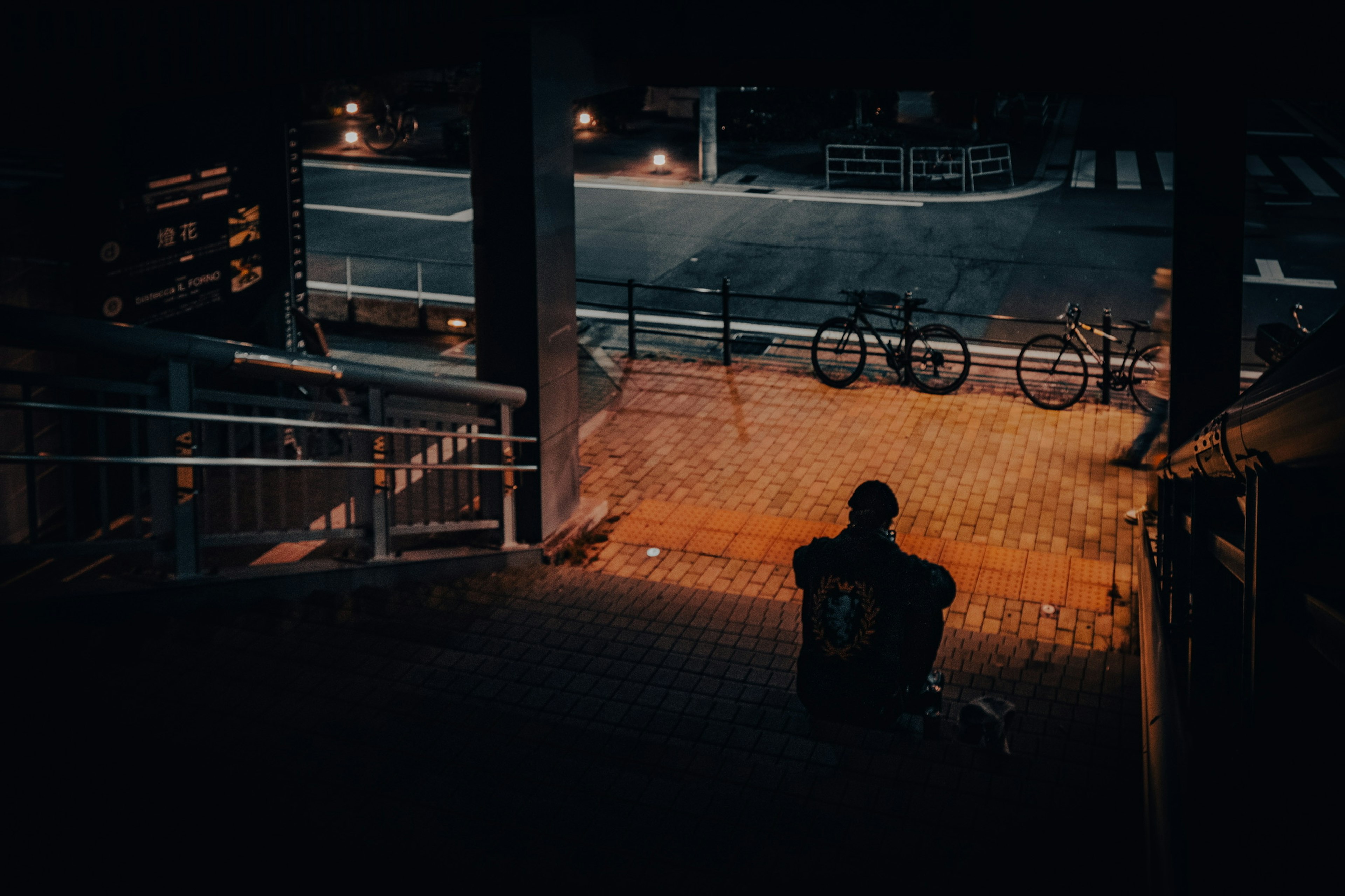 人が階段に座っている夜の街の風景 自転車が背景に見える