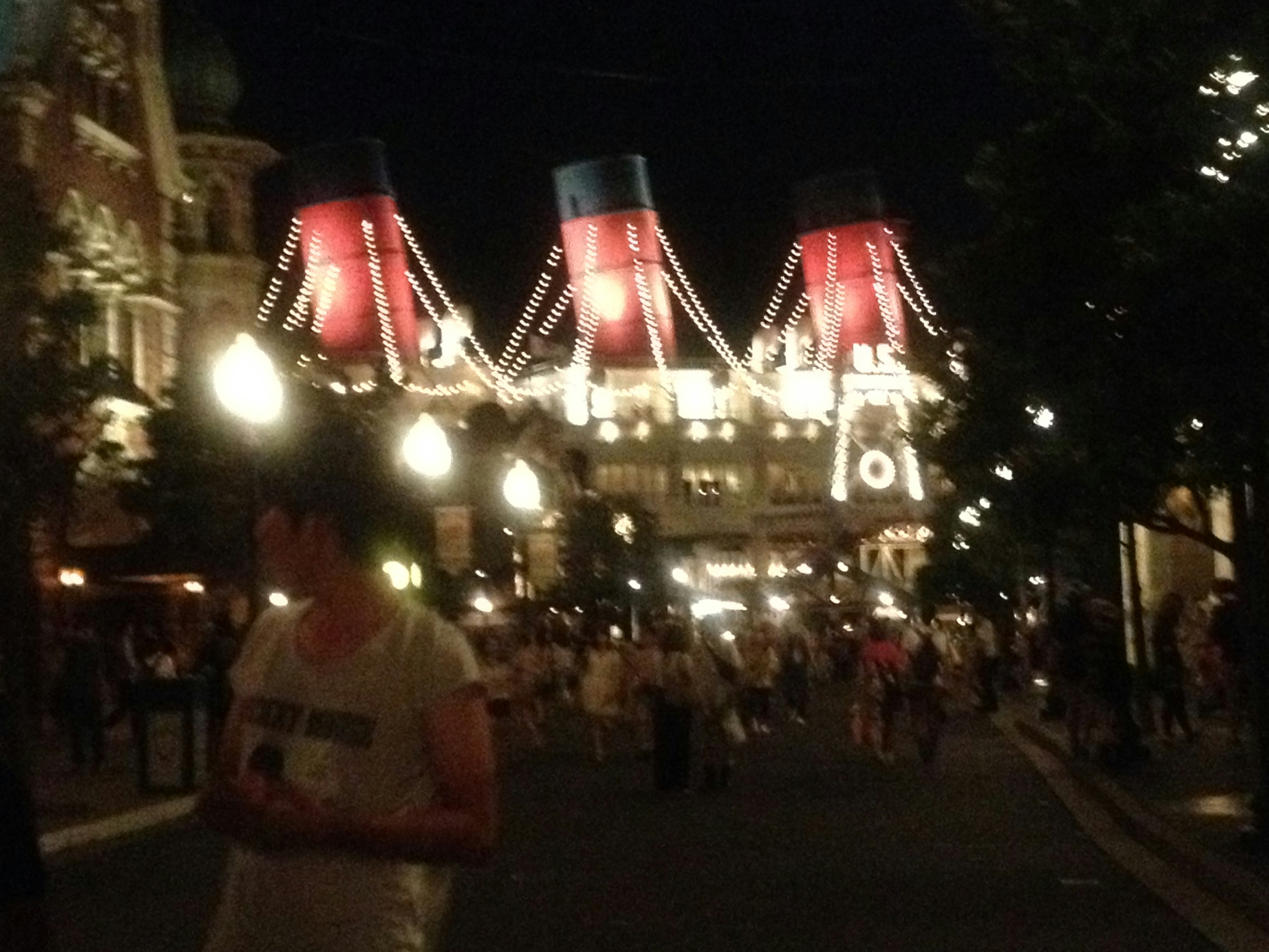 People walking on a lit street with a grand ship design in the background