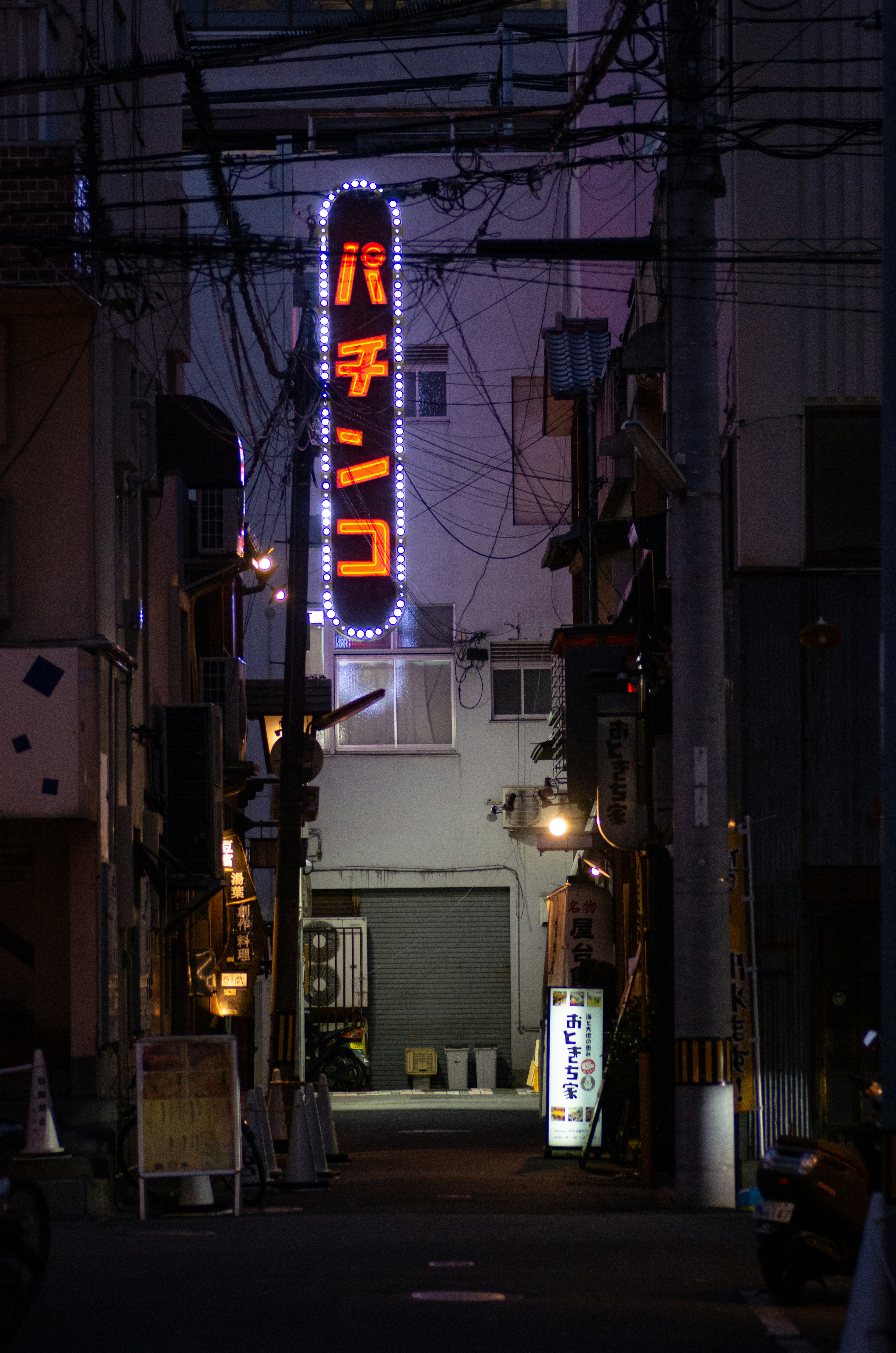 Calle poco iluminada con un letrero de pachinko brillante y cables suspendidos