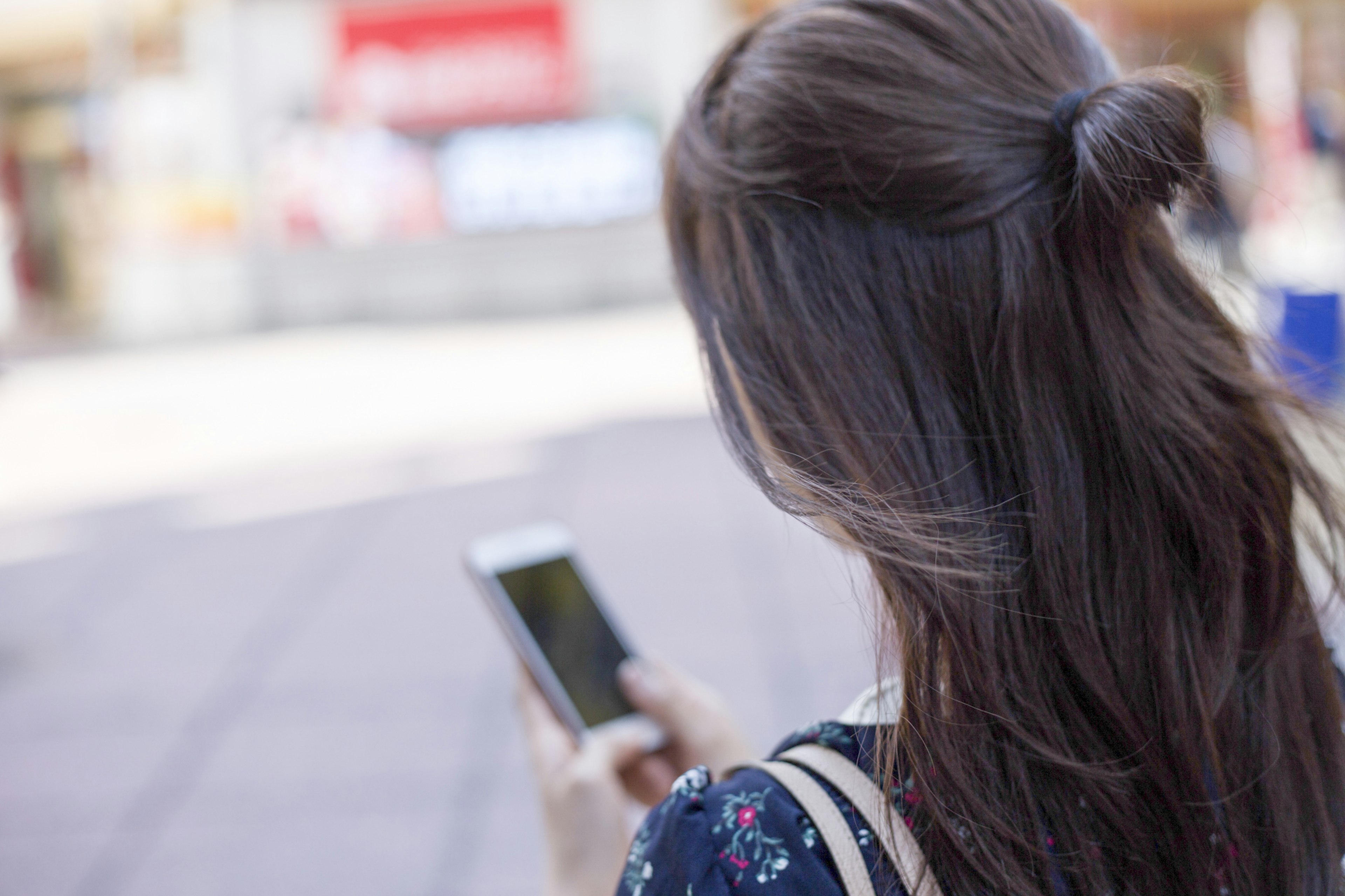 Frau, die ein Smartphone benutzt, von hinten gesehen mit halb hochgestecktem Haar und lässiger Kleidung