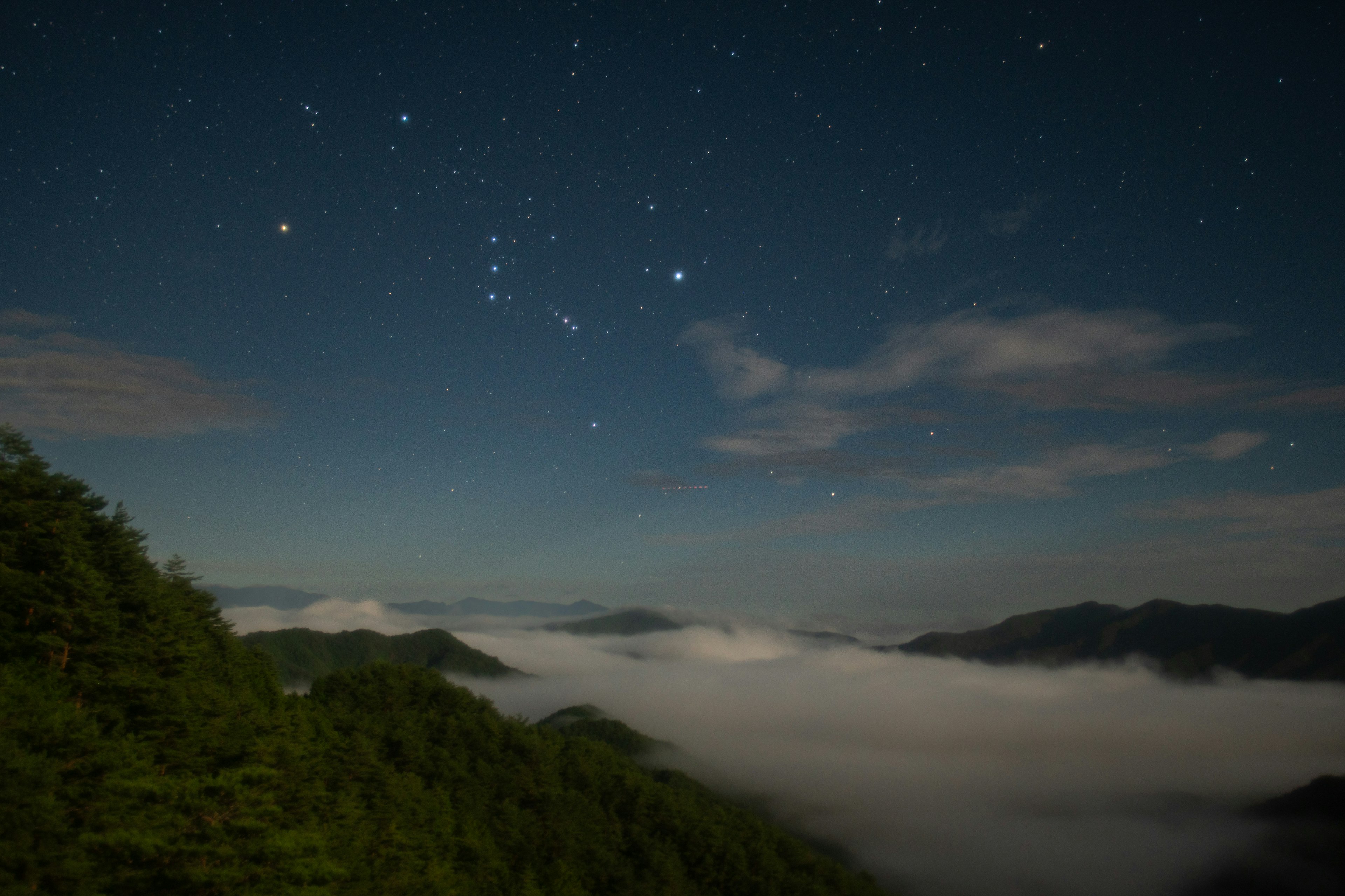 Cielo stellato sopra un mare di nuvole con montagne visibili