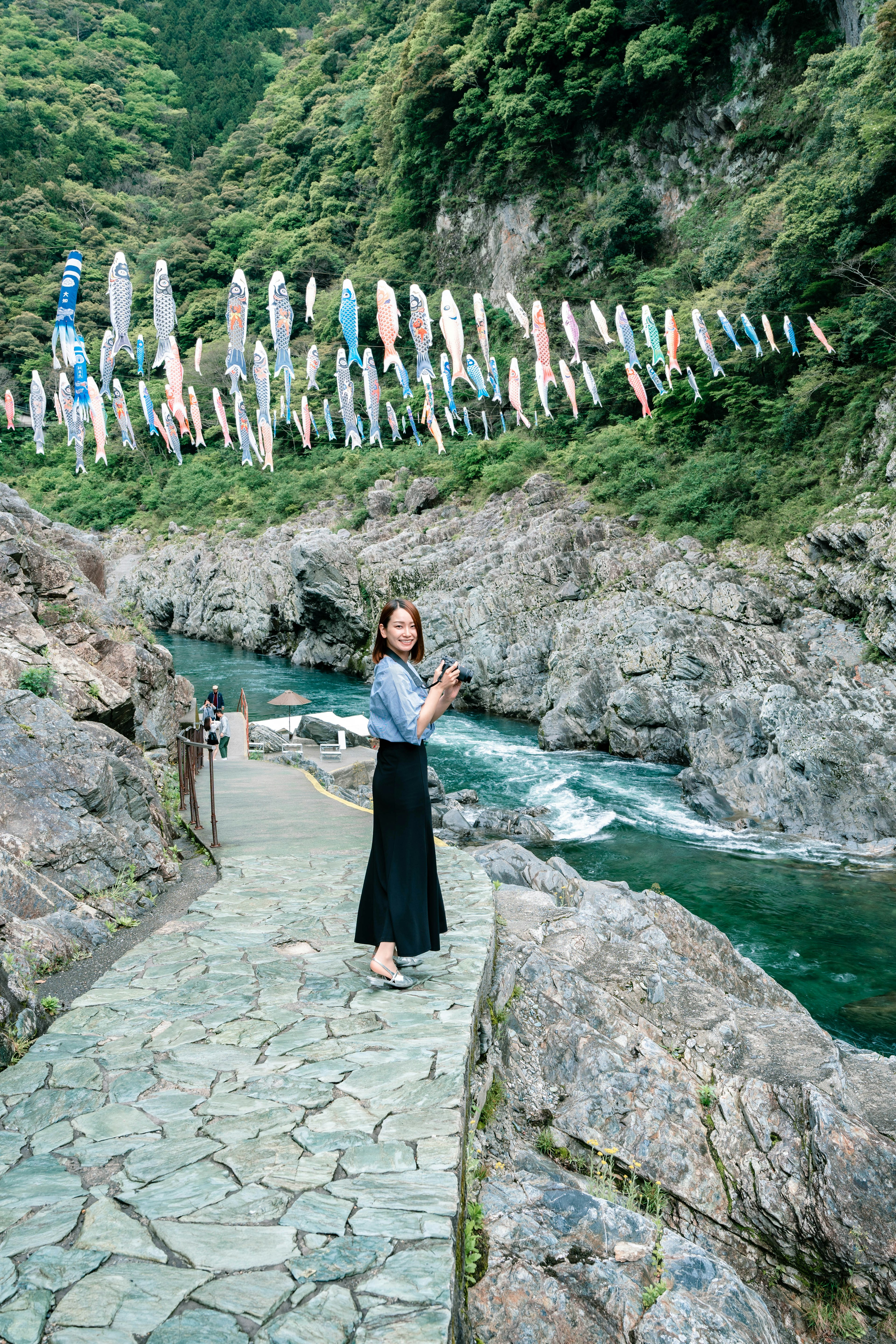 Una mujer de pie junto a un río con banderas de koi coloridas colgadas arriba