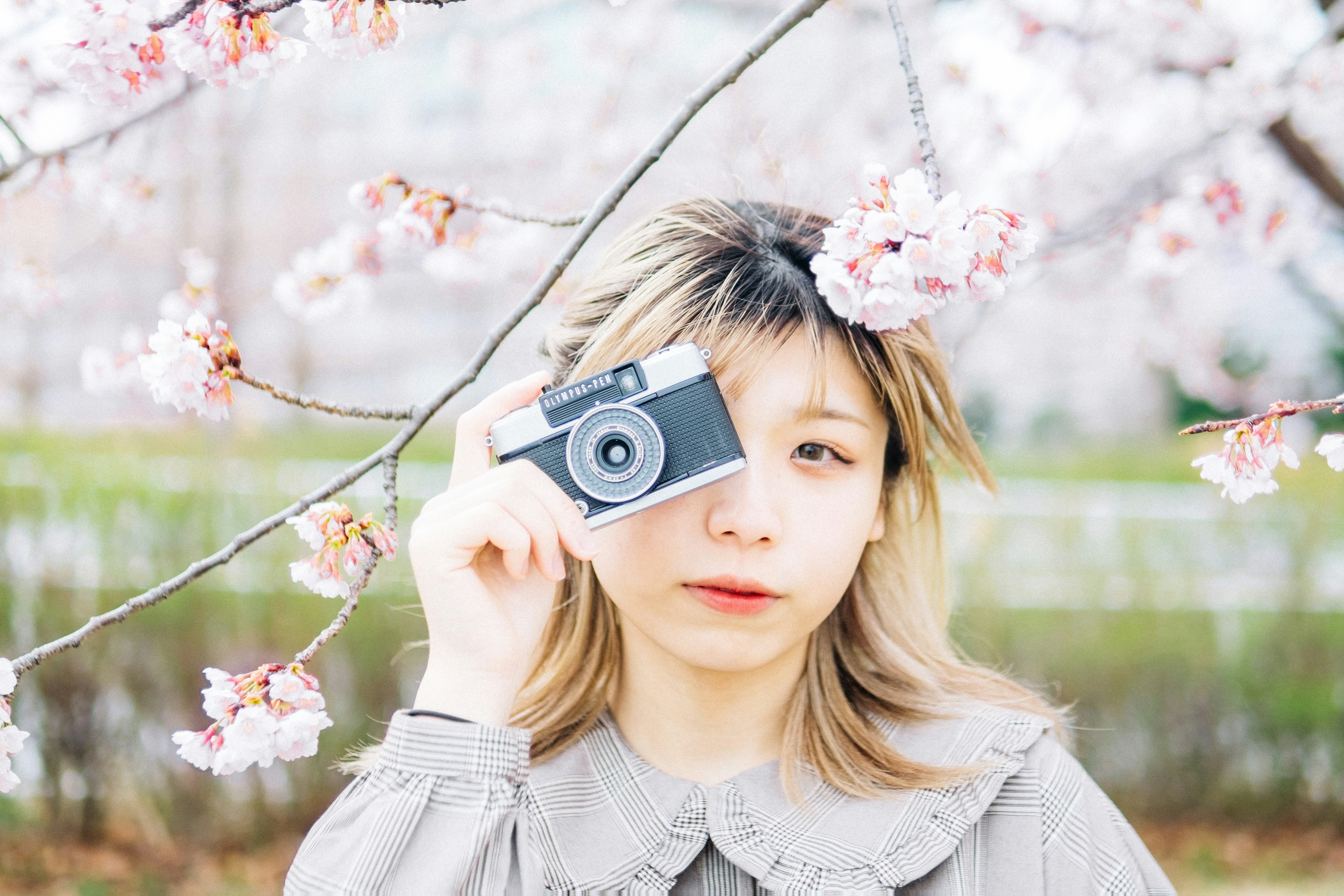 A woman holding a camera in front of cherry blossom trees