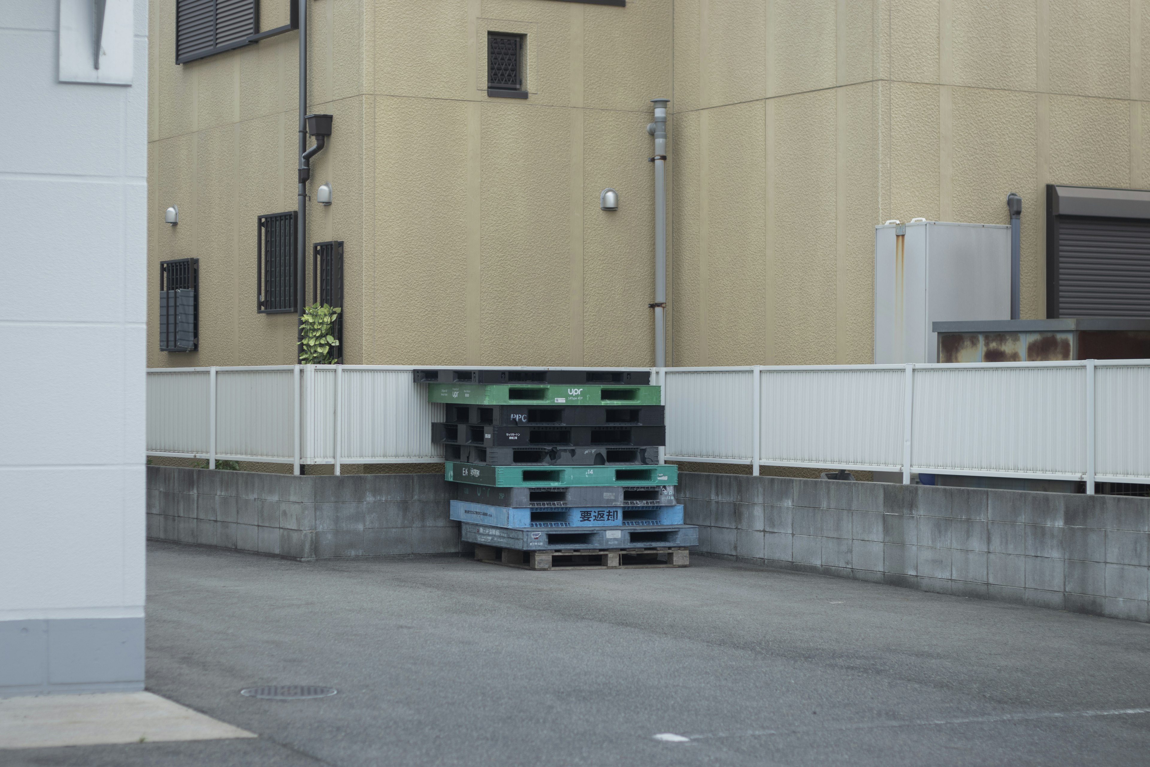 Stack of blue and green pallets behind a warehouse