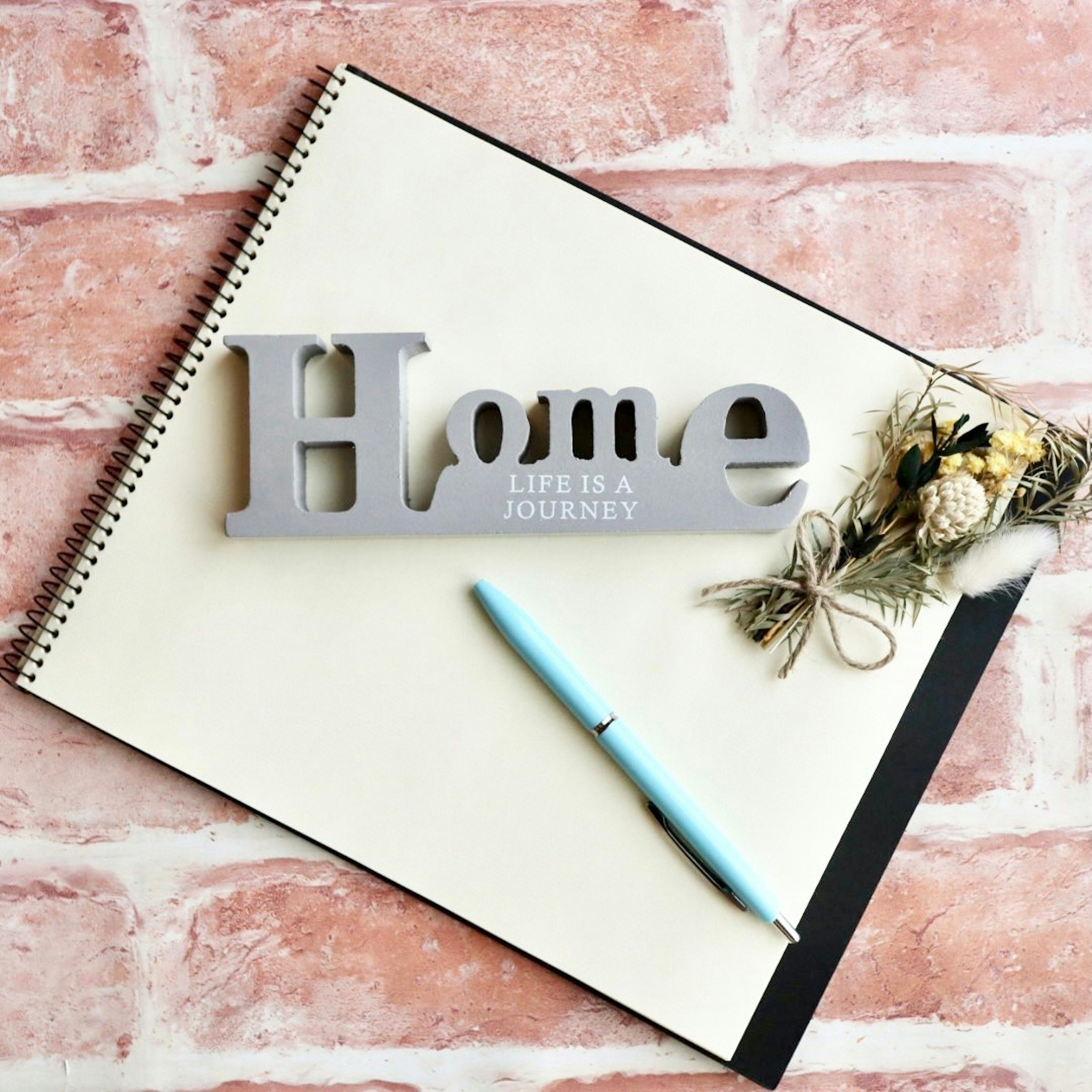 Decorative 'Home' sign on a notepad with a blue pen and dried flowers