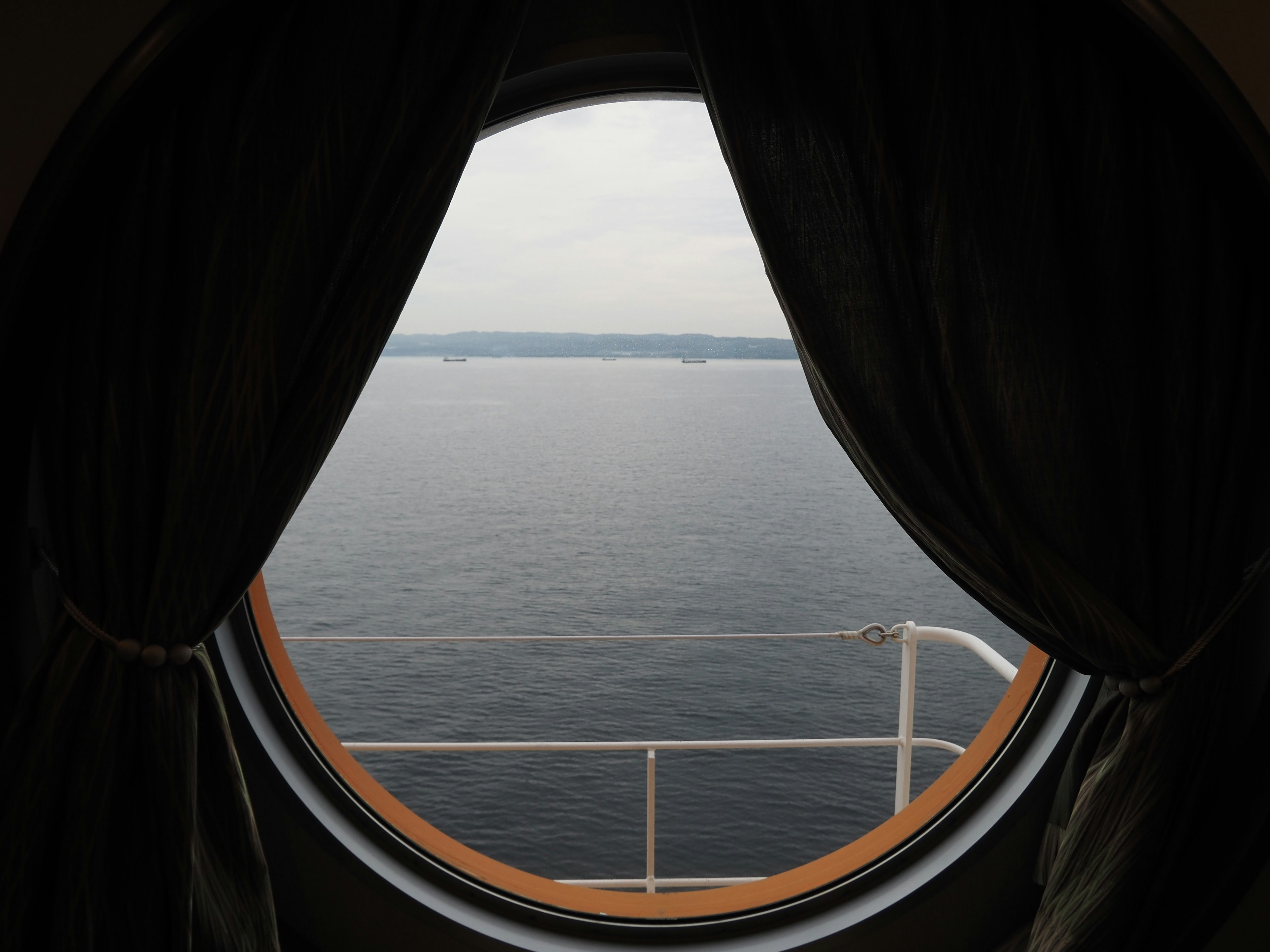 Circular window revealing a calm sea view with curtains drawn aside