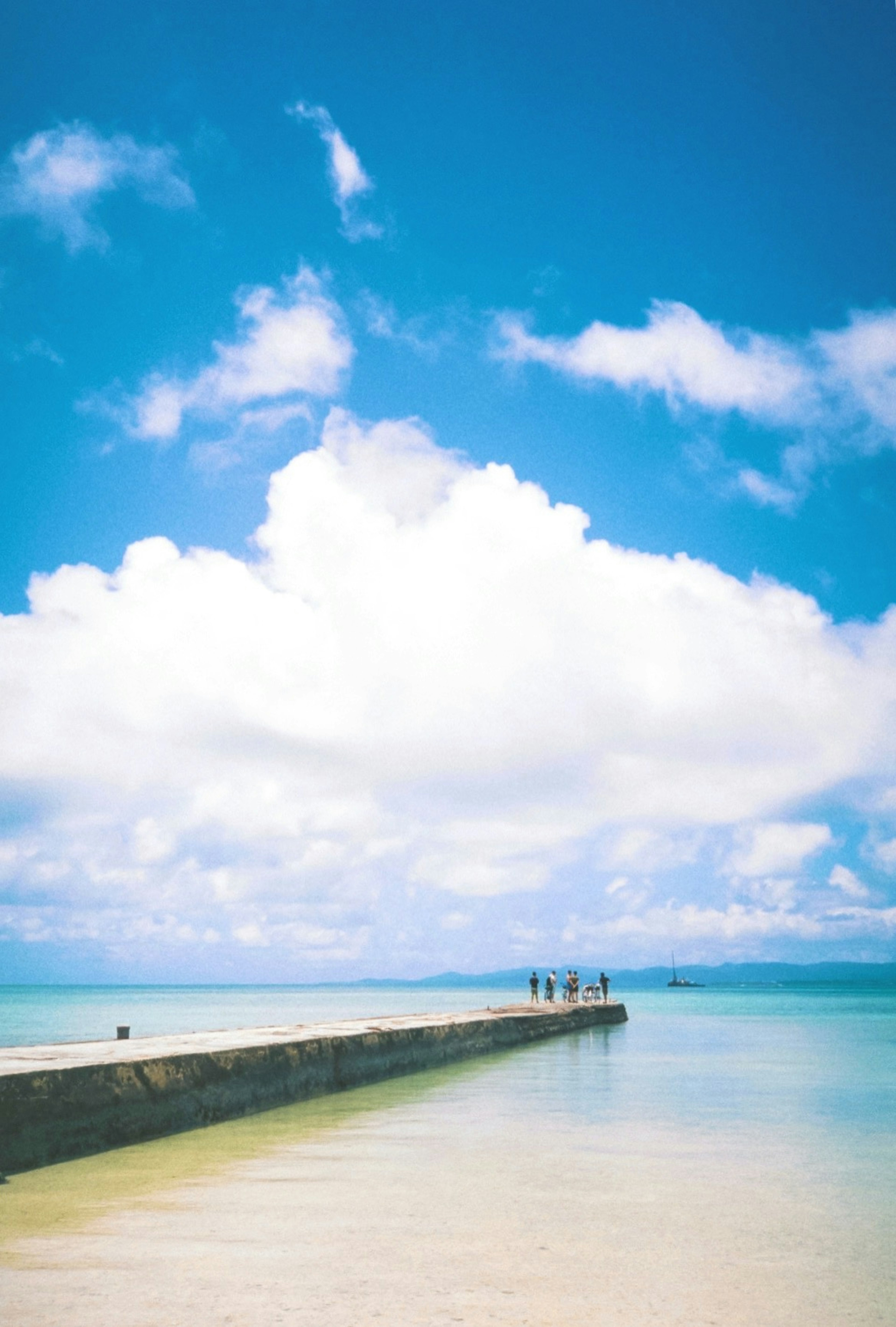 Jetée côtière sous un ciel bleu avec des nuages blancs et des gens