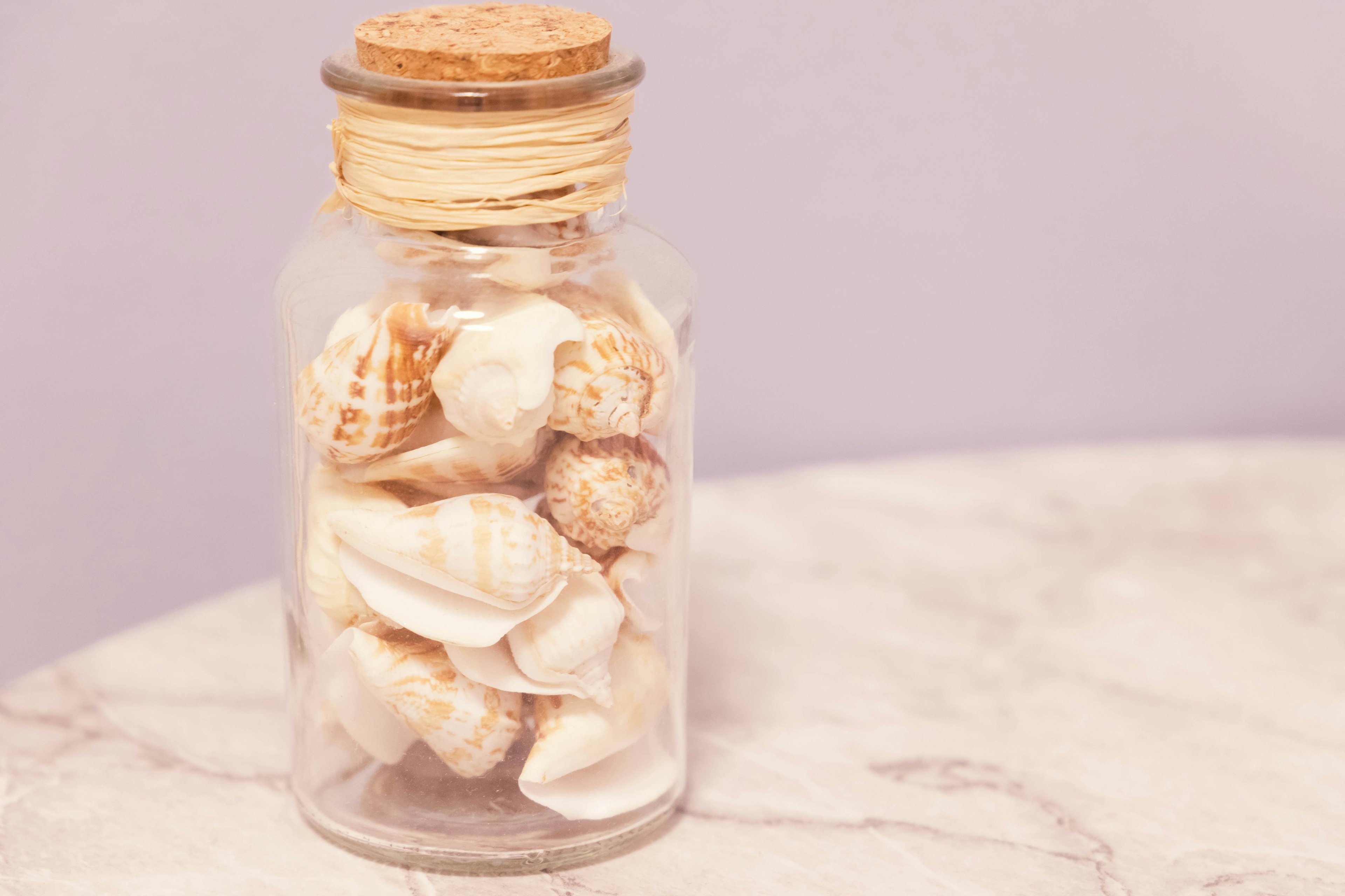 A glass jar filled with seashells on a marble surface