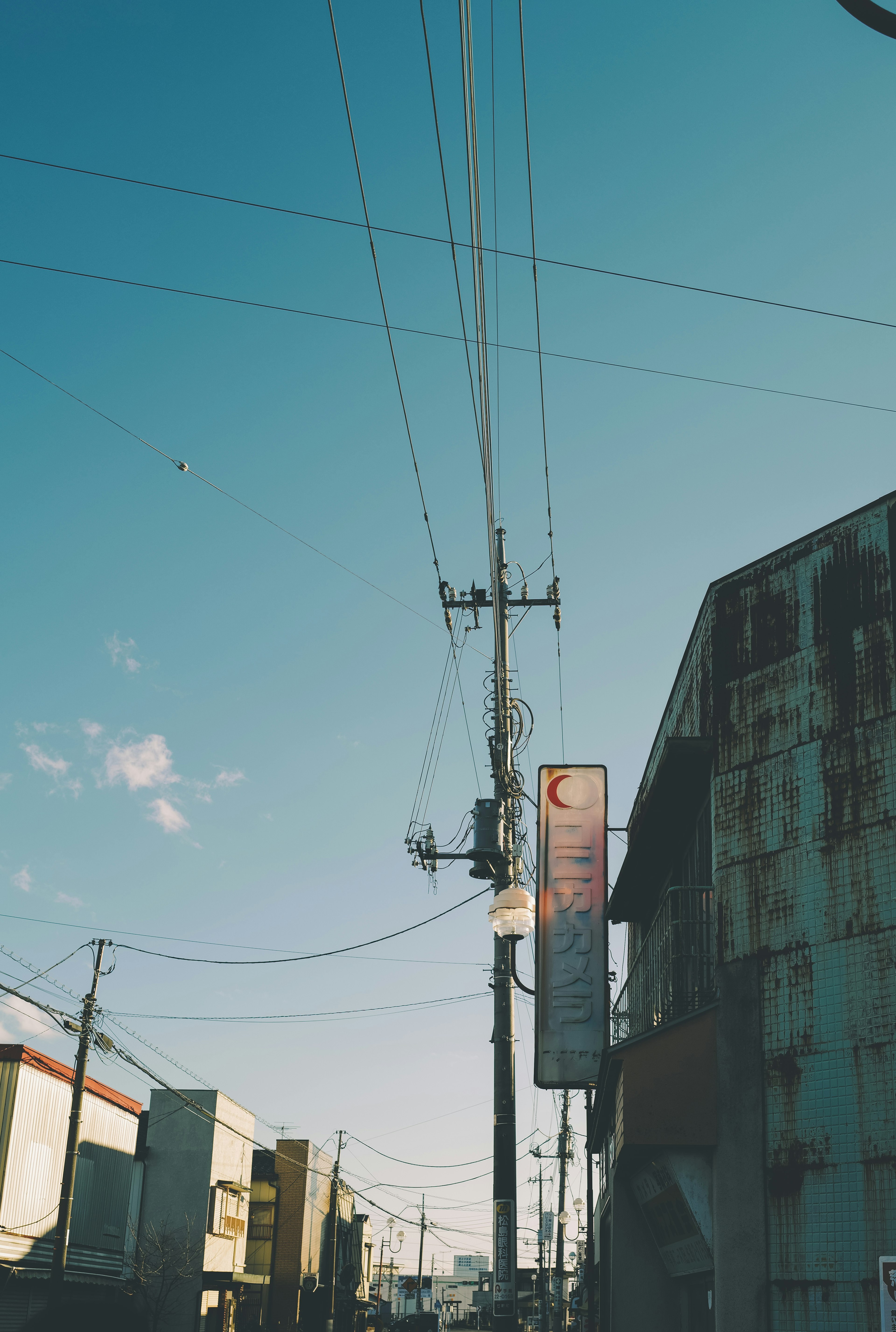 Escena urbana con un poste de servicios públicos y líneas eléctricas bajo un cielo azul