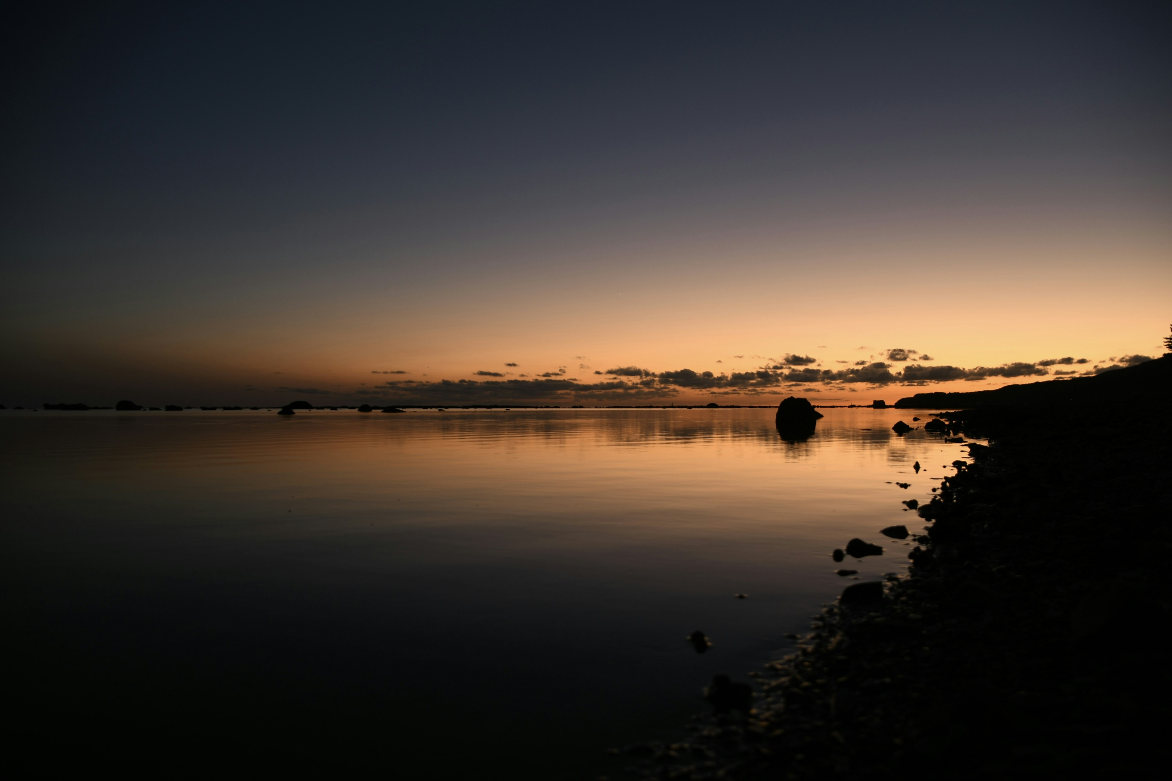 静かな海の夕暮れの風景、穏やかな水面と暗い岸辺