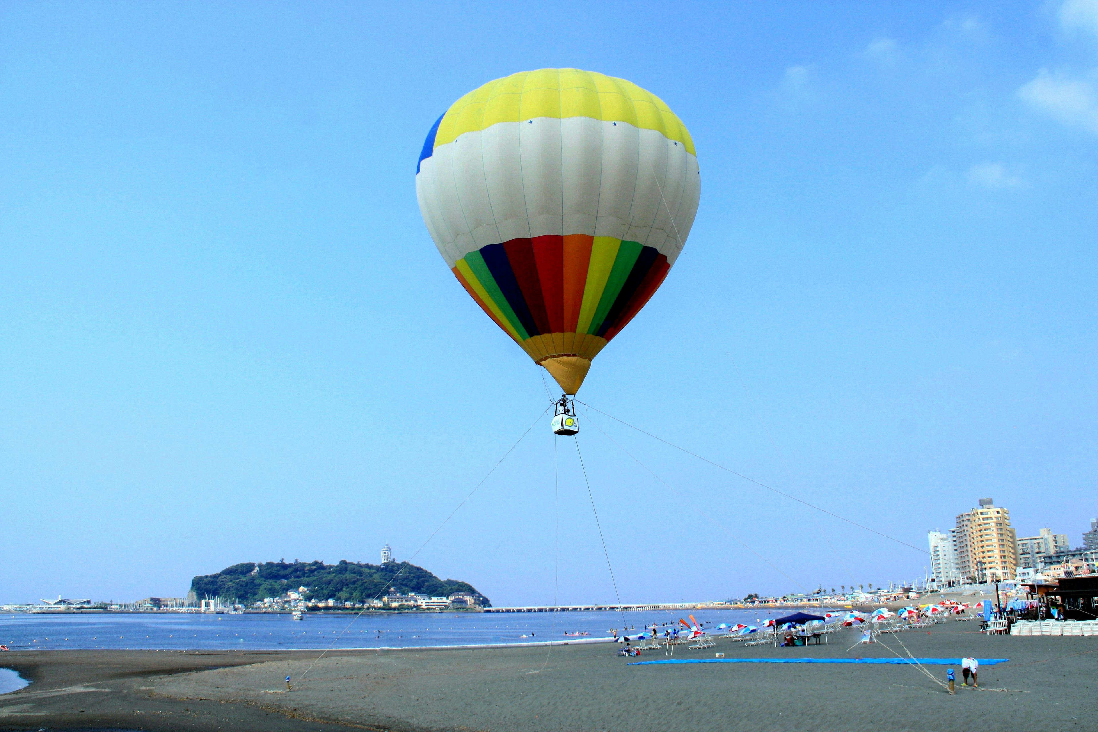 Pallone aerostatico colorato che fluttua vicino al mare sotto un cielo blu