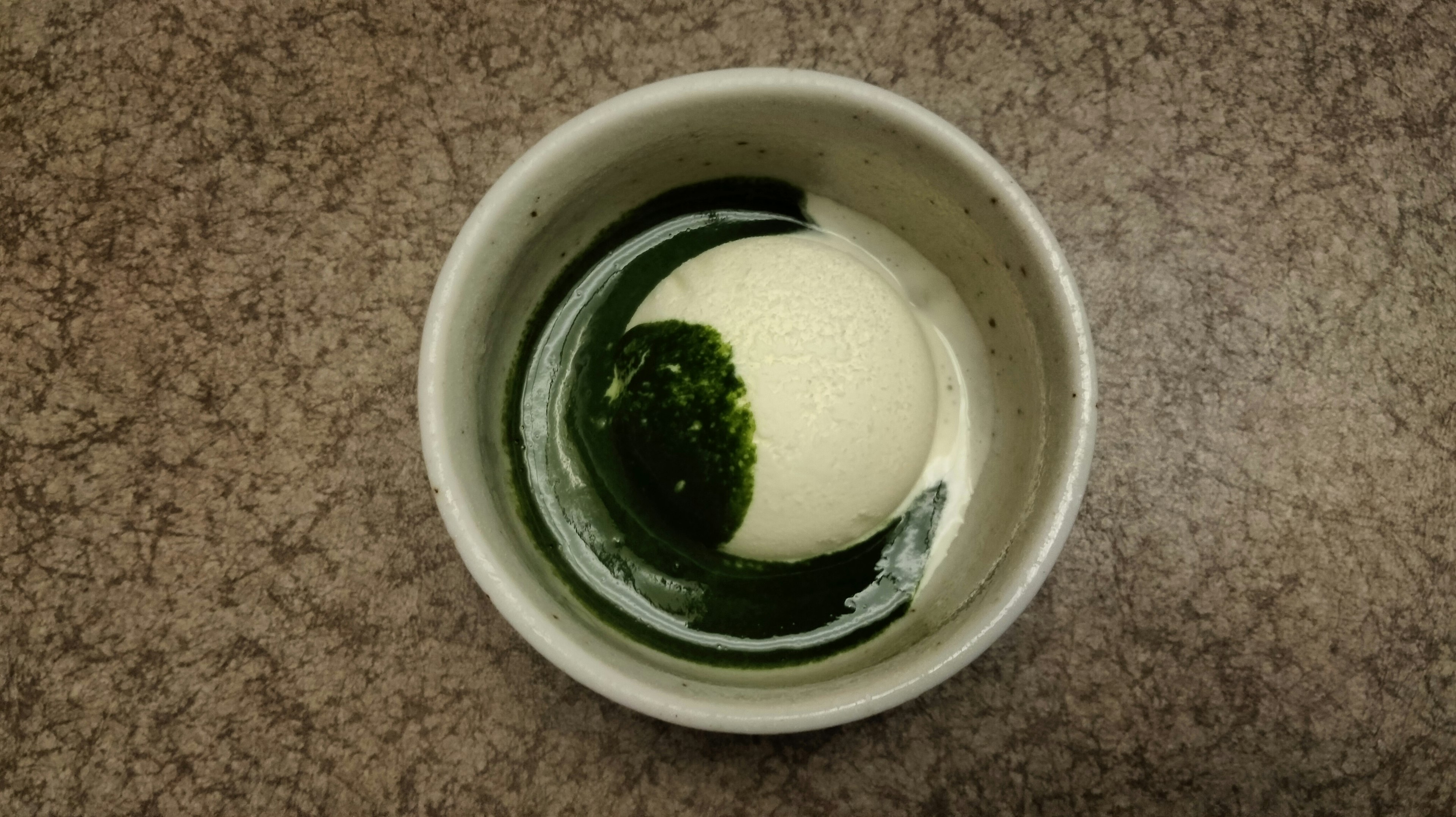 A small bowl containing white ice cream and green sauce