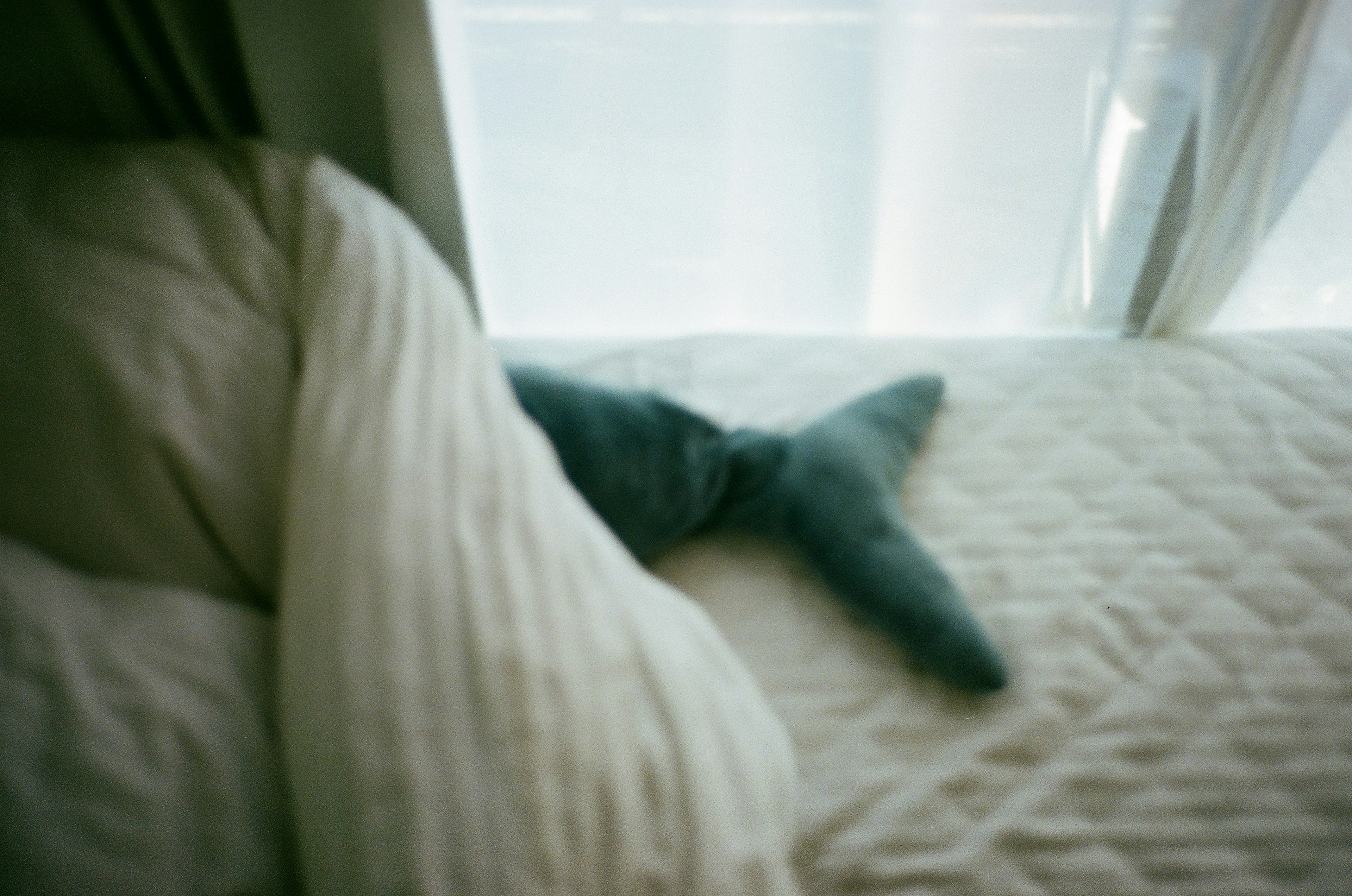 Image of a blue cushion resembling a fish tail on a bed with white bedding