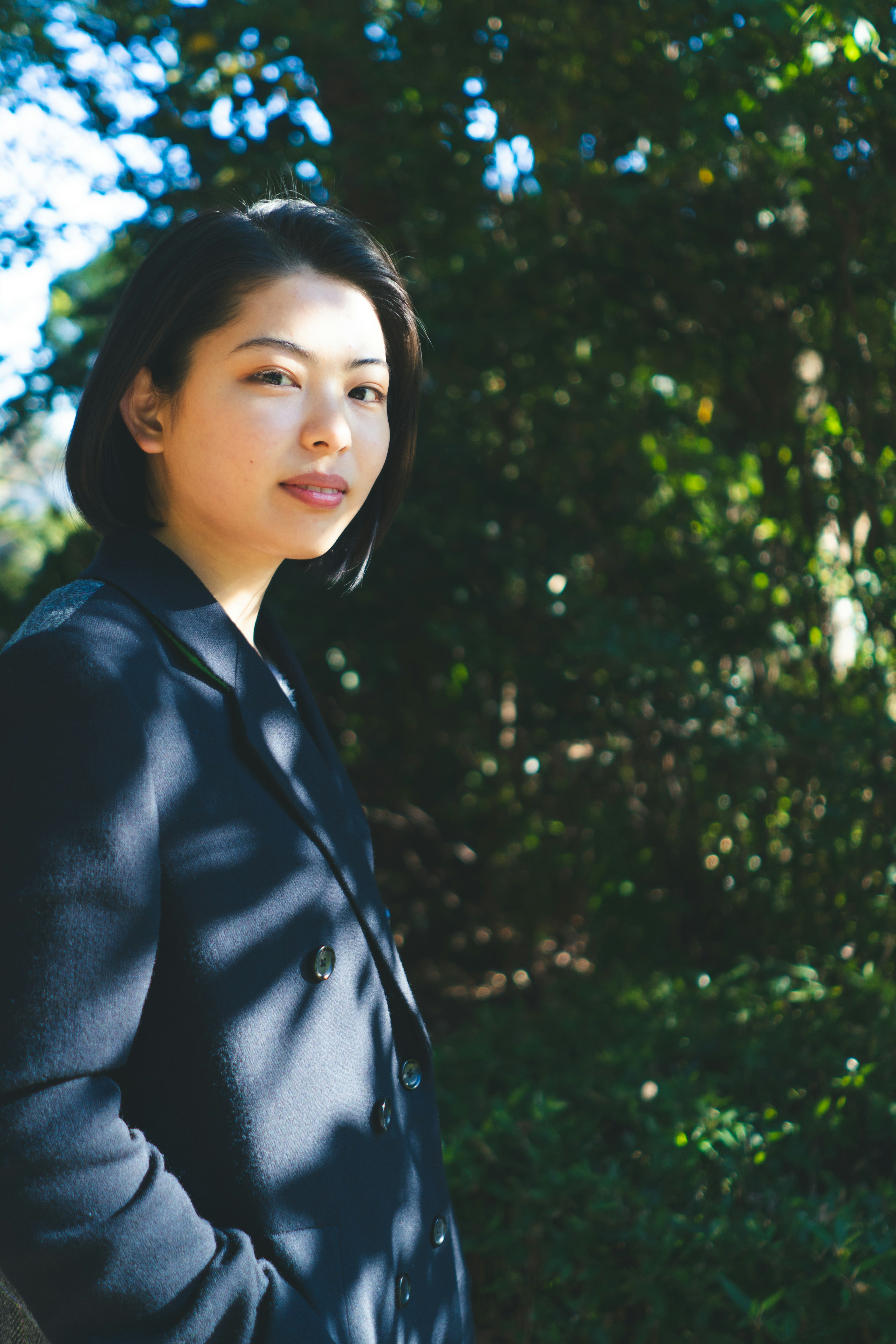 Portrait of a woman standing amidst green foliage Bright sunlight illuminating her face