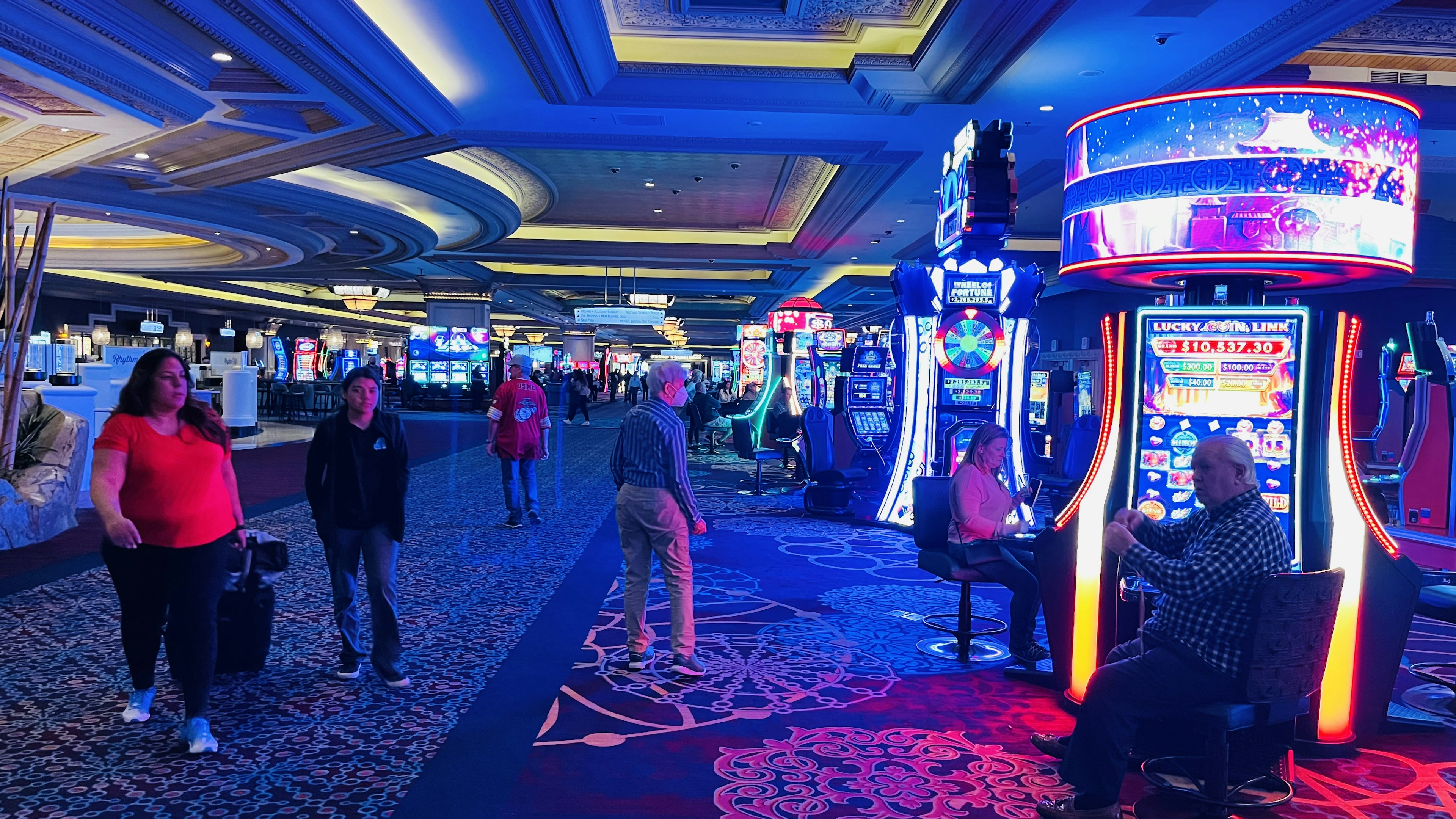 Persone che camminano in un casinò con slot machine colorate e illuminazione blu