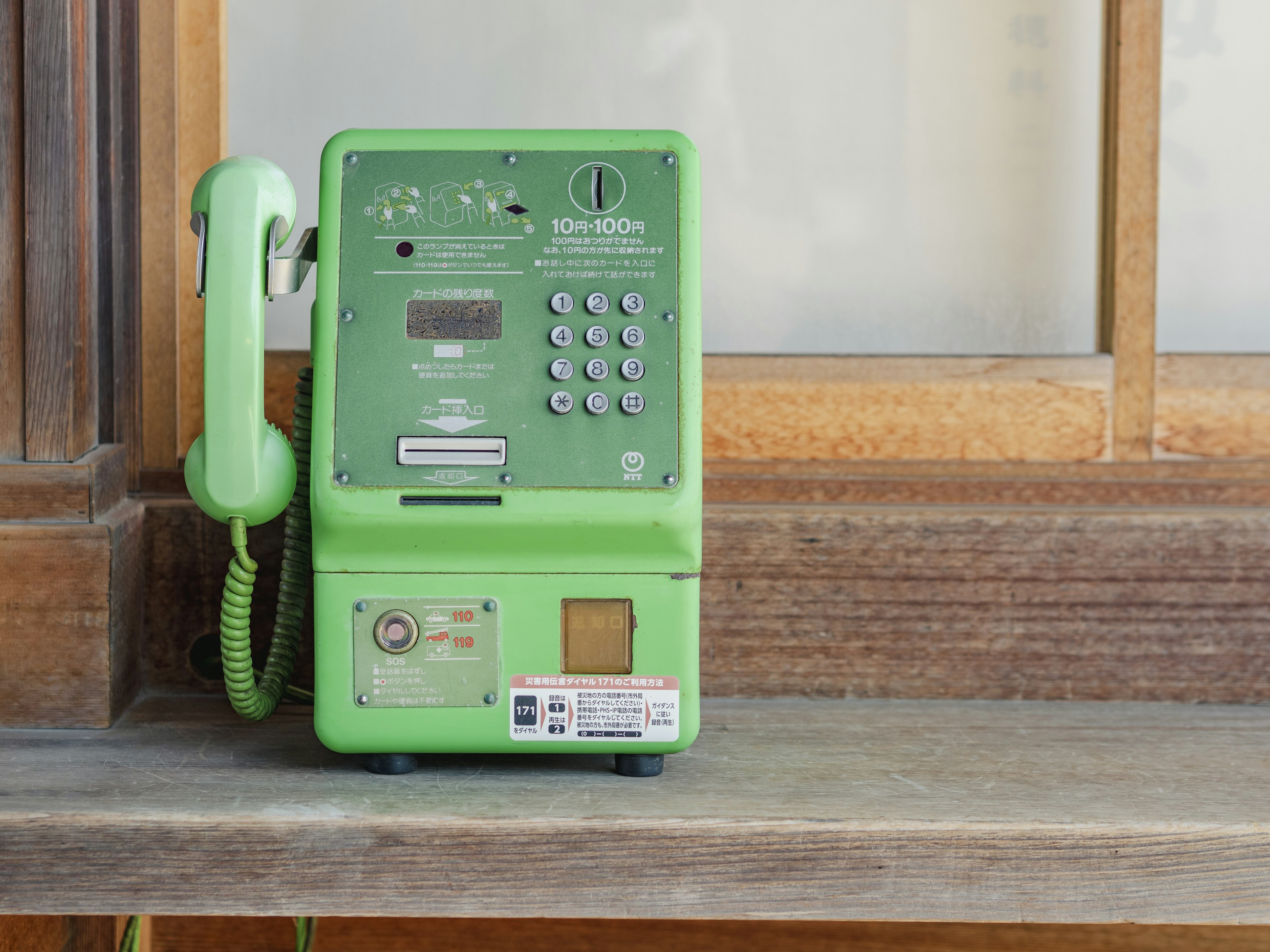 Teléfono público verde colocado sobre una estantería de madera