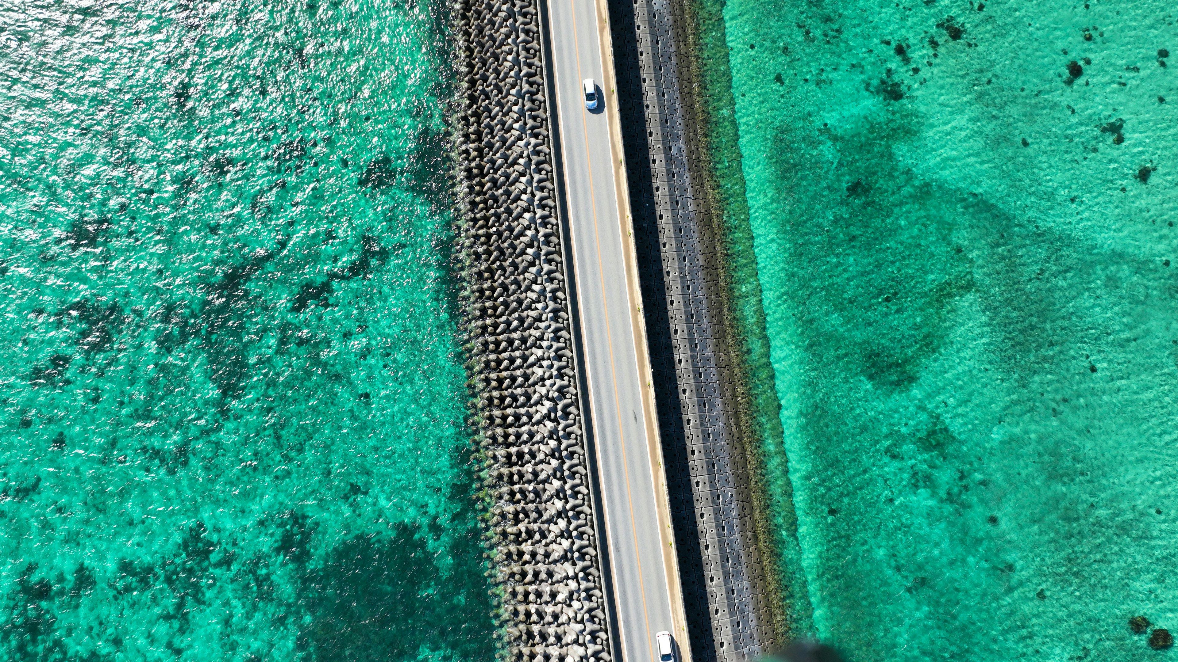 青い海の上にある白い道路と石の堤防が見える空撮