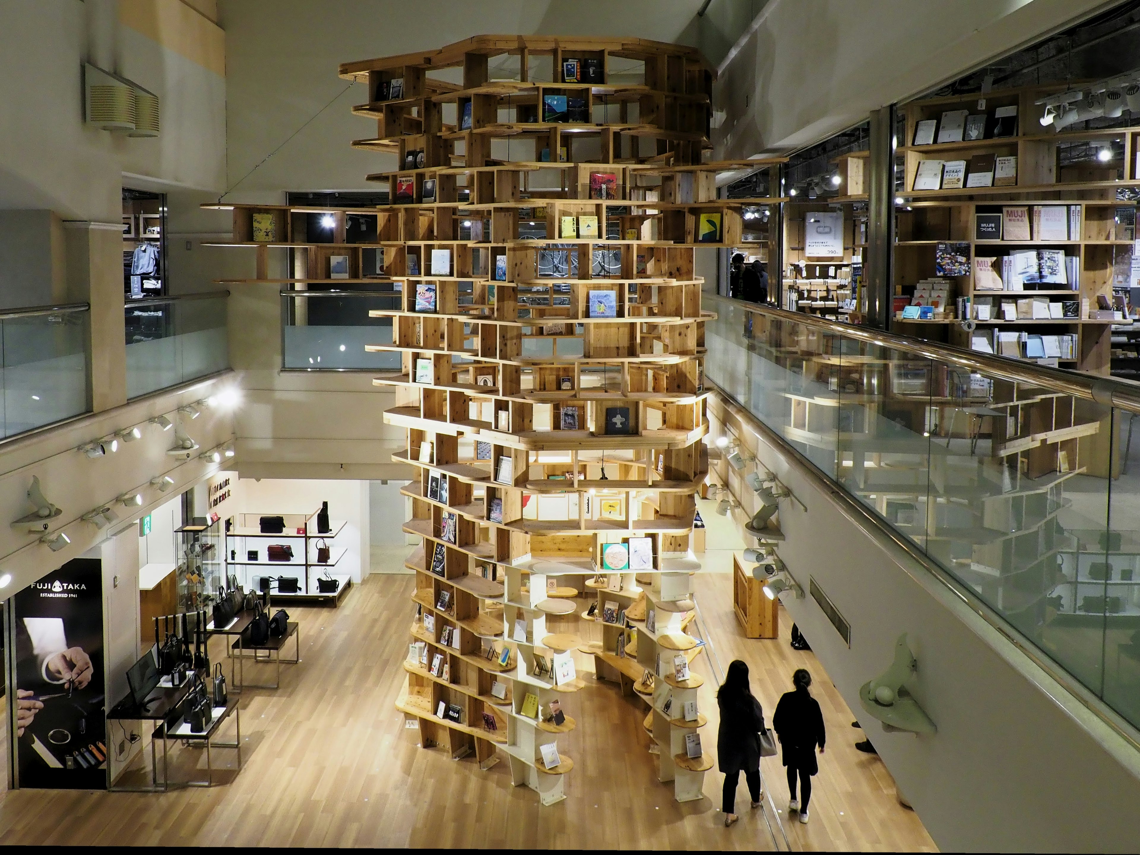 Interior of a modern bookstore featuring a unique wooden bookshelf structure two people standing near the bookshelf