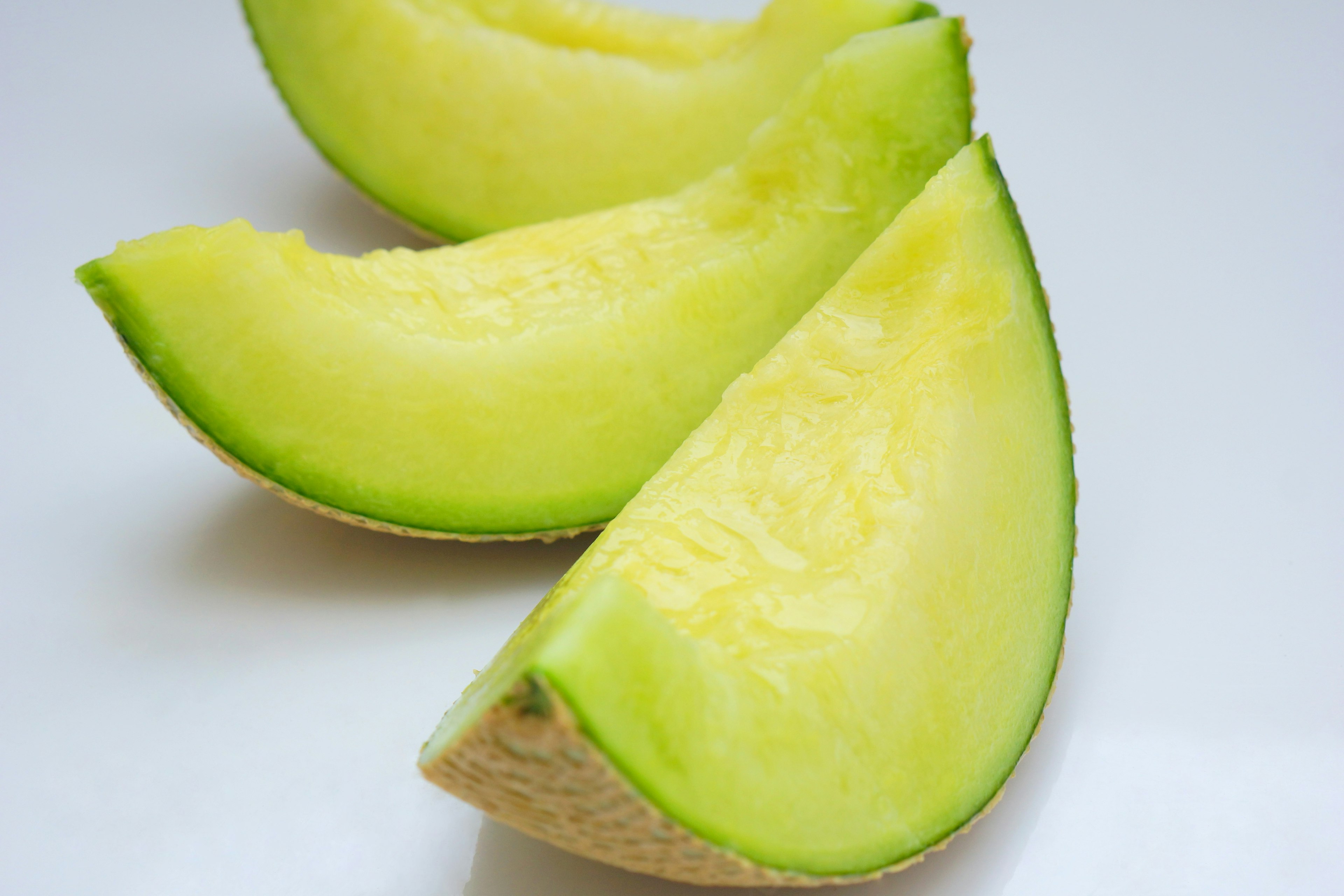 Three slices of melon with green flesh arranged on a white background