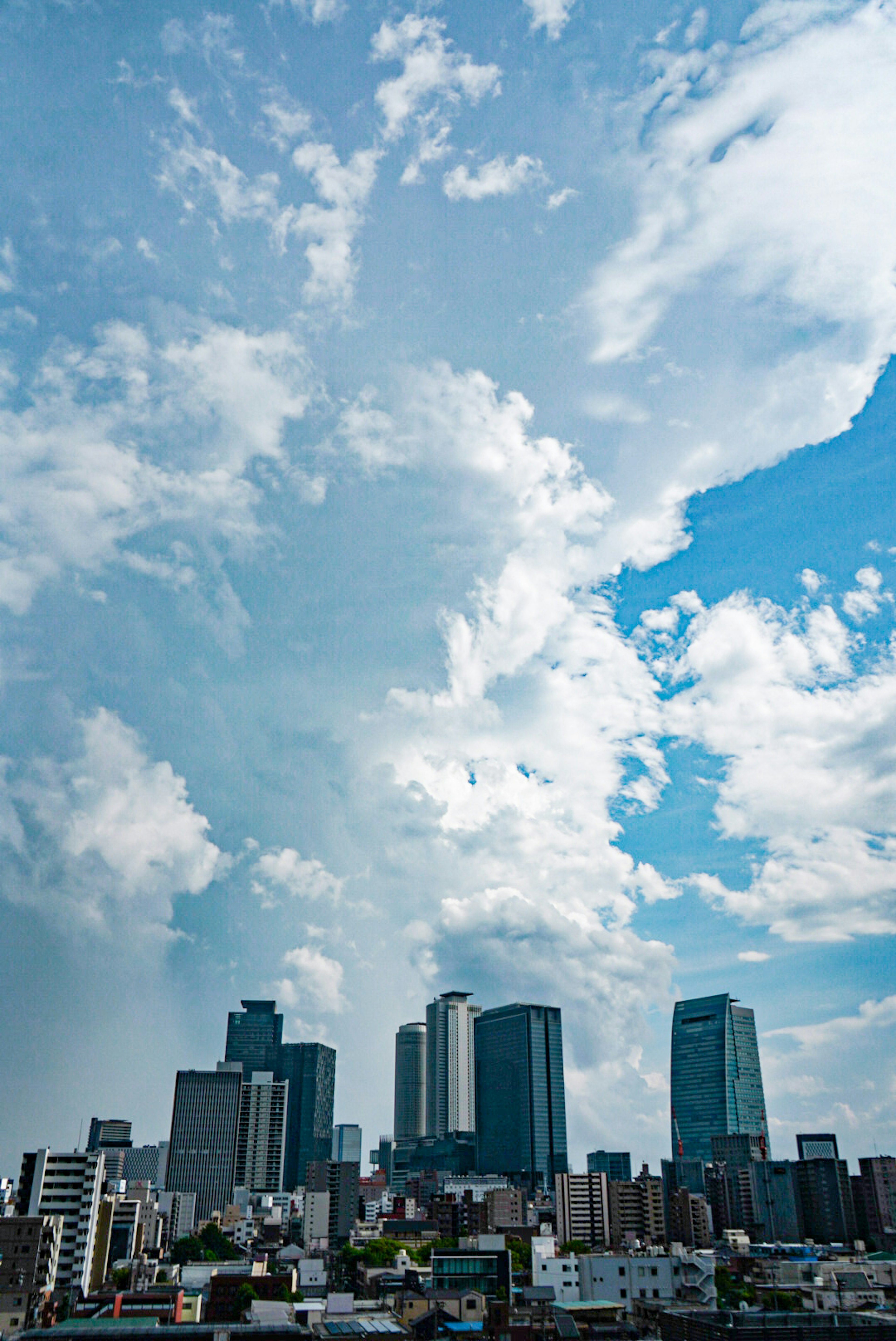 Skyline di una città con grattacieli sotto un cielo azzurro e nuvole bianche