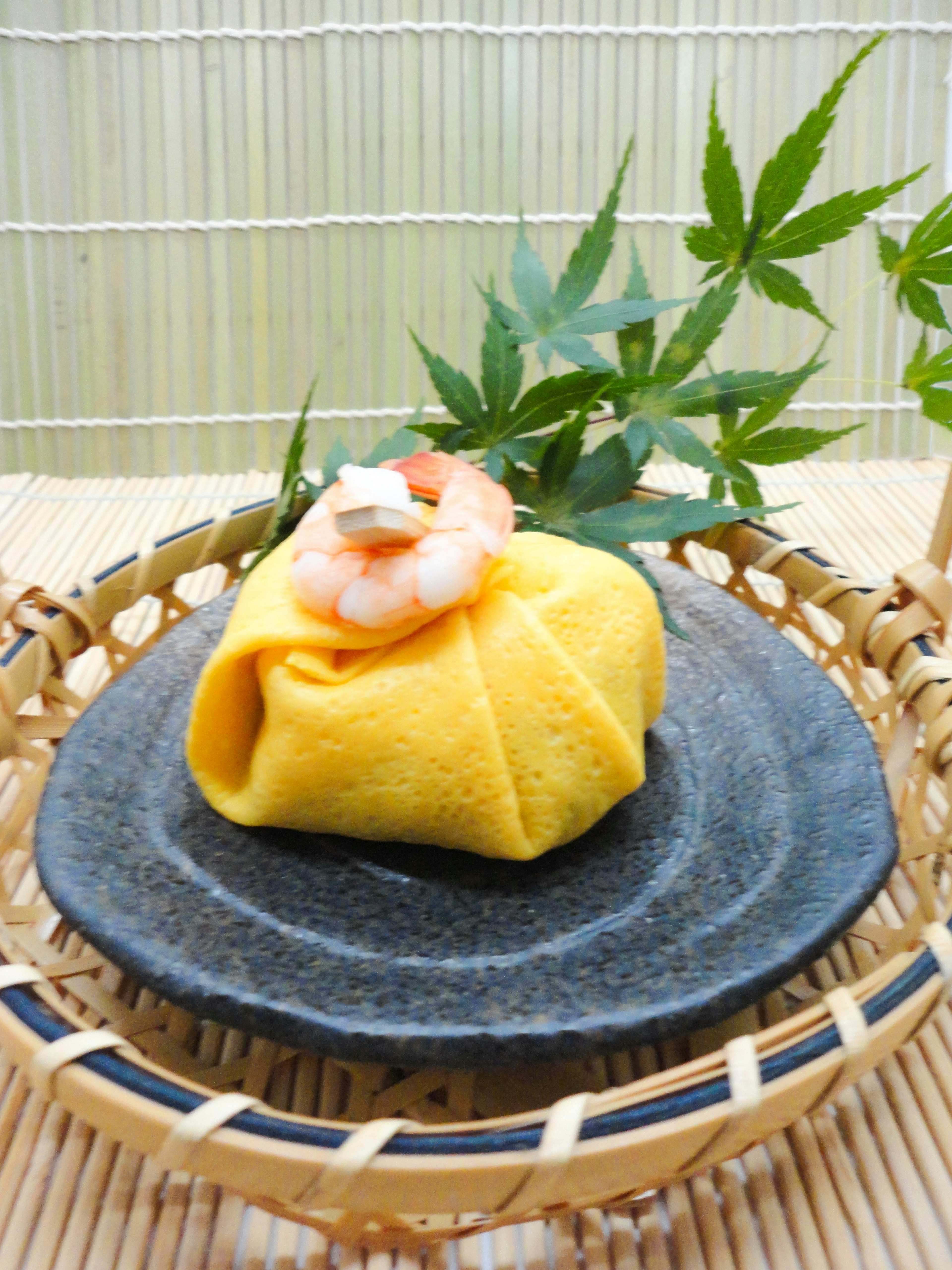 Beautiful Japanese wagashi with a yellow wrap topped with shrimp and leaves