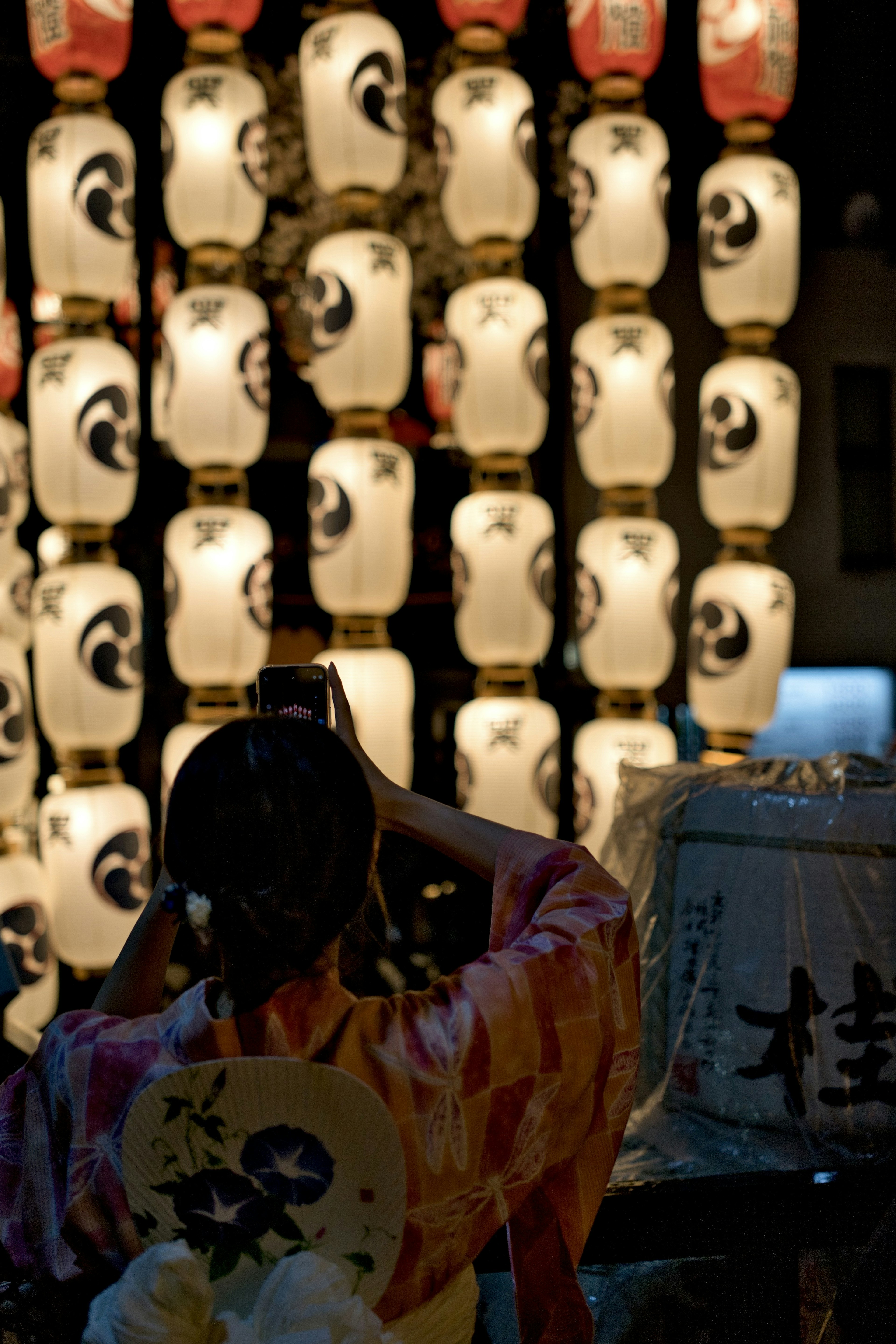 Woman in a kimono photographing lanterns at a night festival