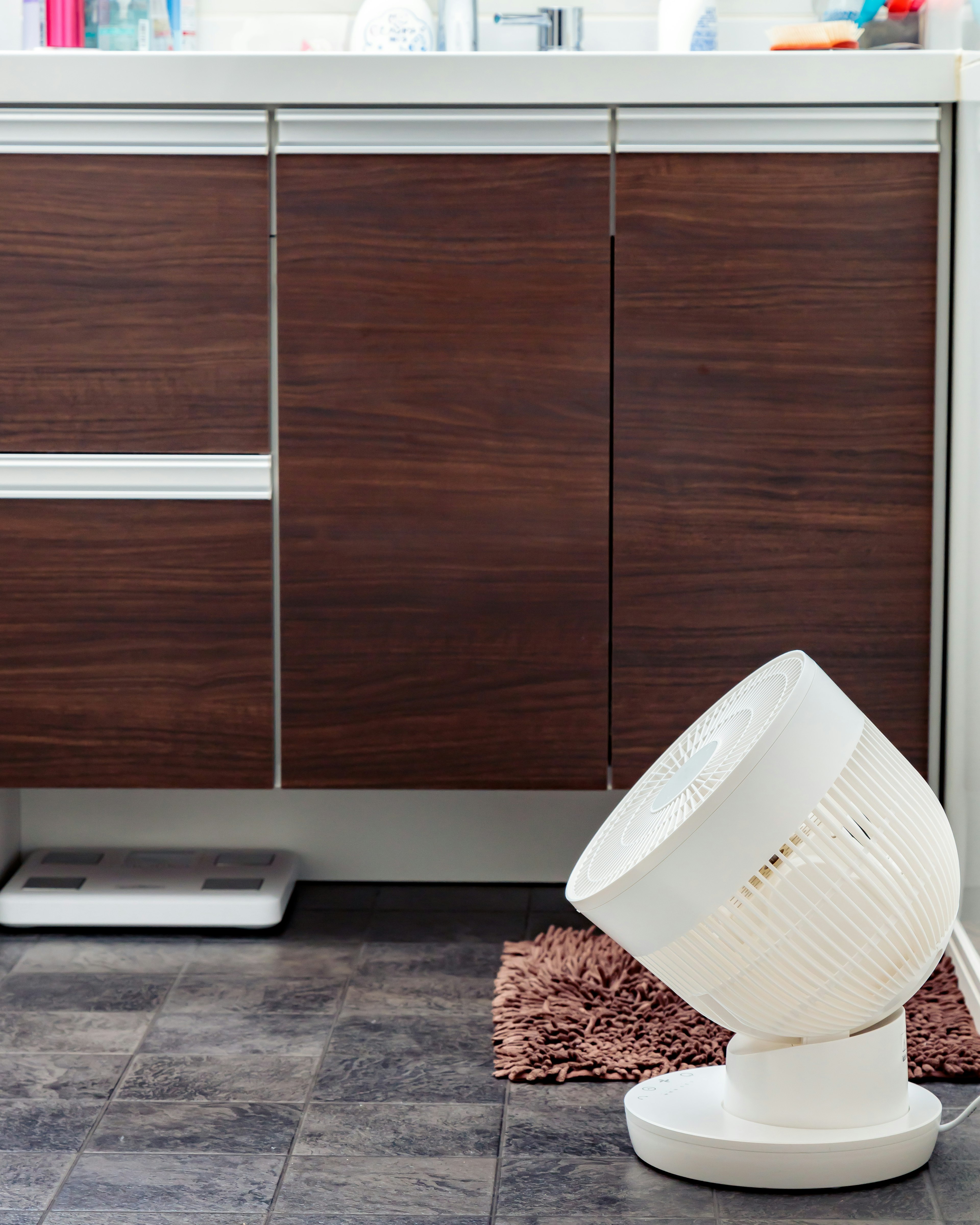 Un ventilatore bianco inclinato in una cucina con armadi in legno e un tappeto