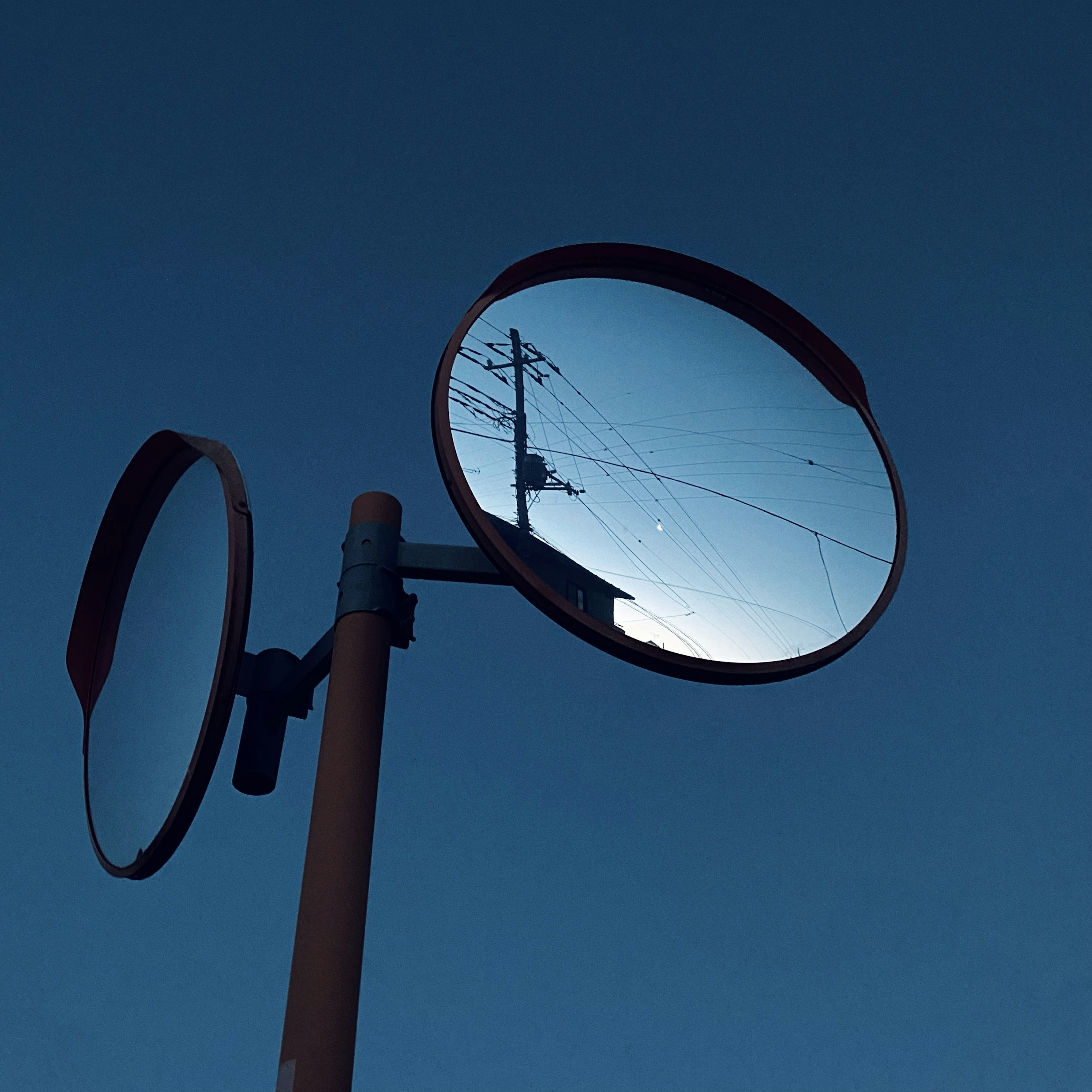 Due specchi convessi che riflettono un cielo blu e un palo della luce