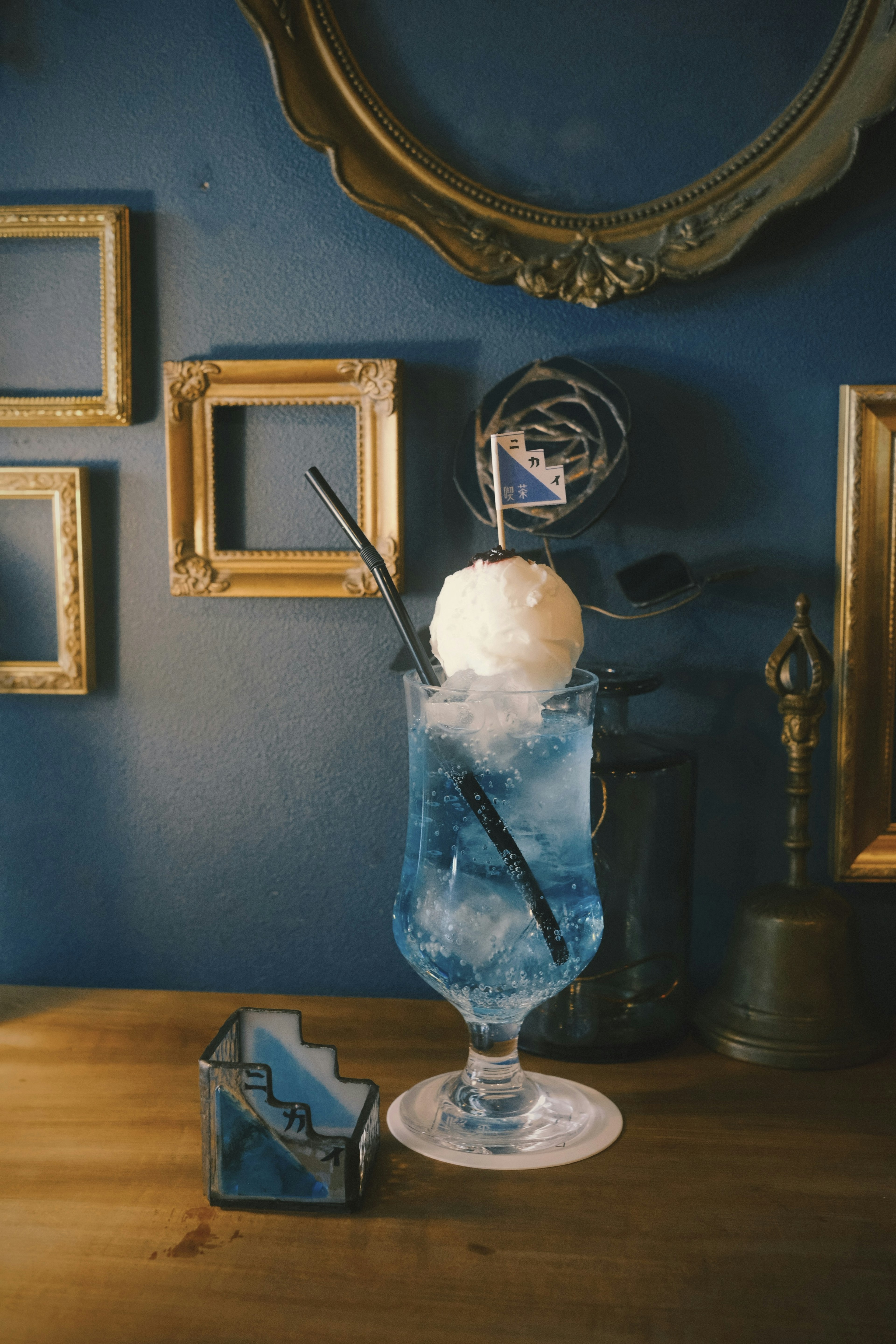 A blue cocktail glass topped with ice cream featuring a decorative straw and surrounded by golden frames