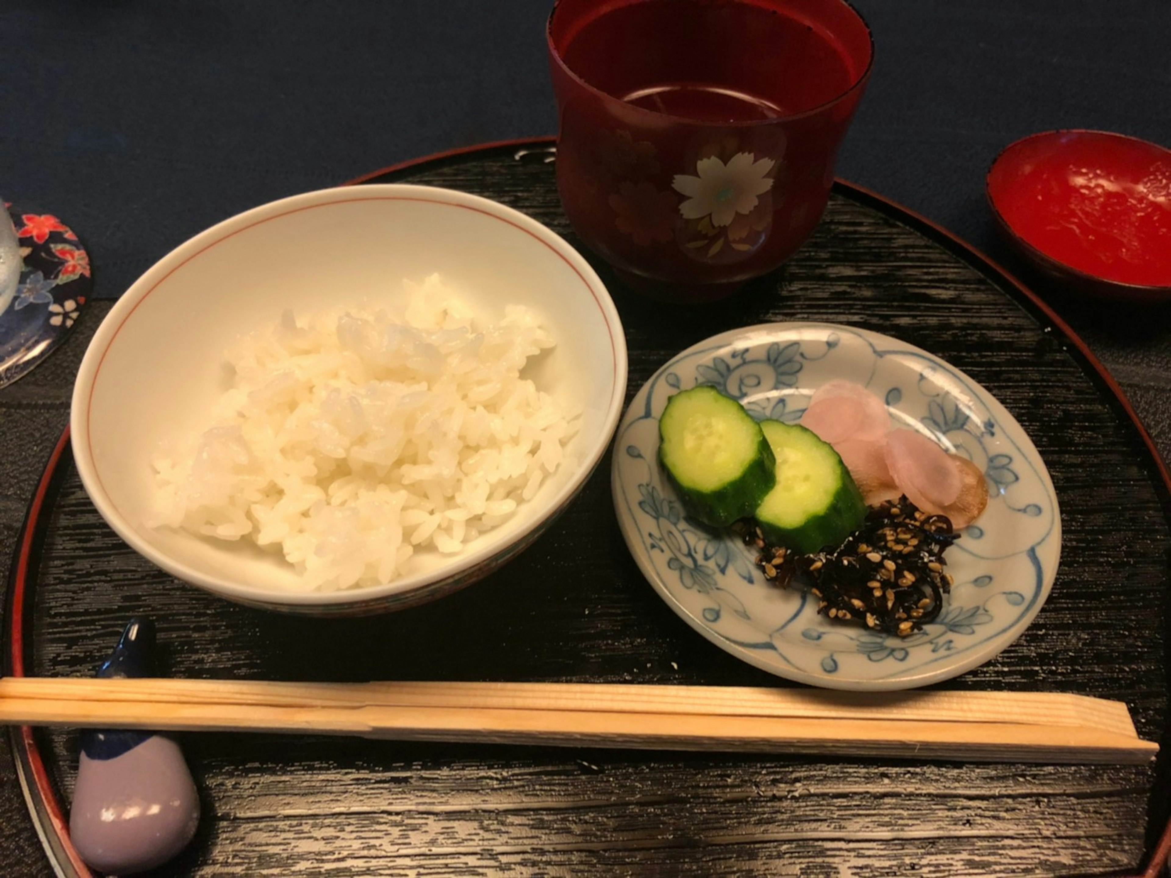 Une assiette avec du riz blanc, des concombres et du jambon, accompagnée d'une tasse de thé rouge