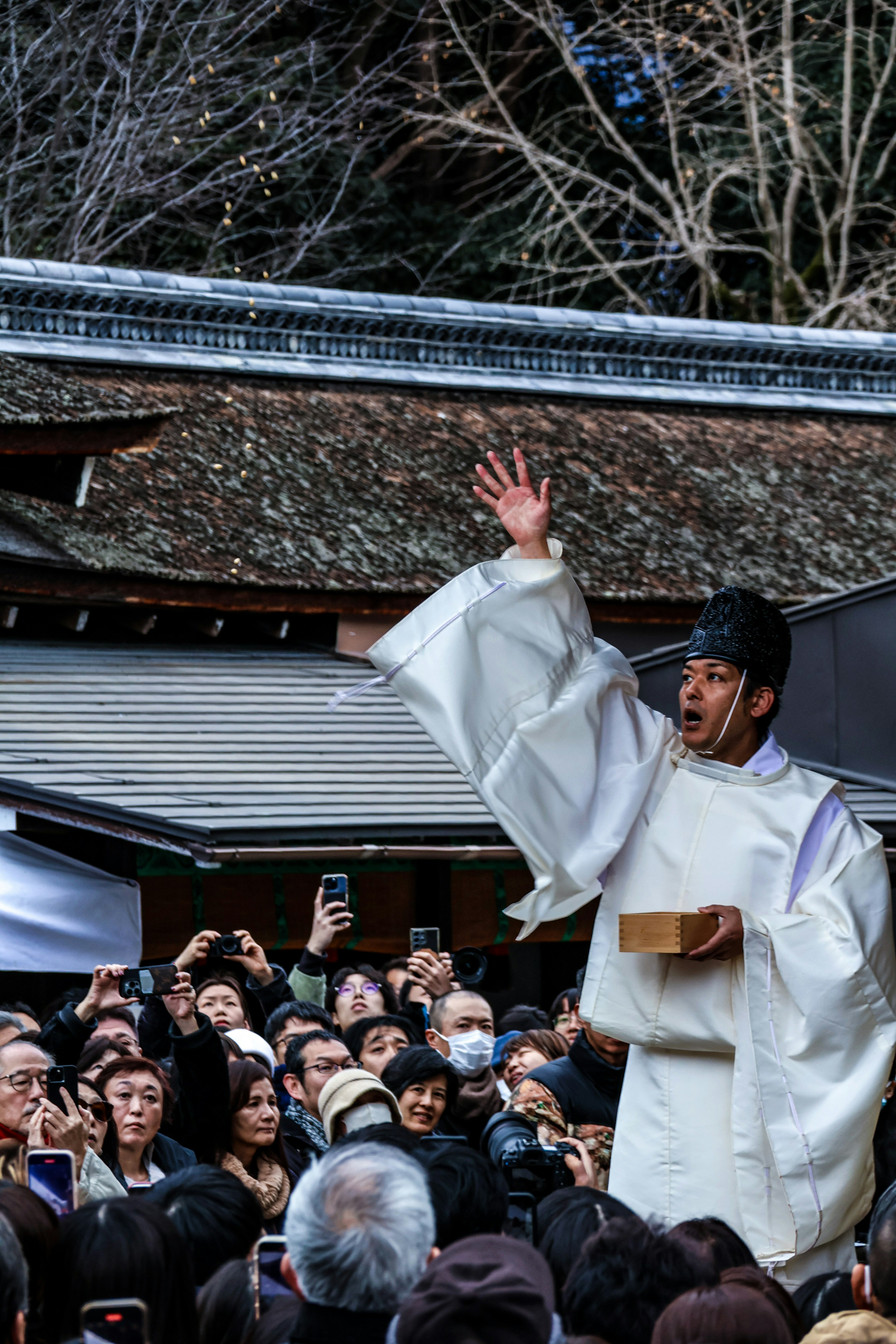 A man in white ceremonial clothing raises his hand during a ritual at a shrine