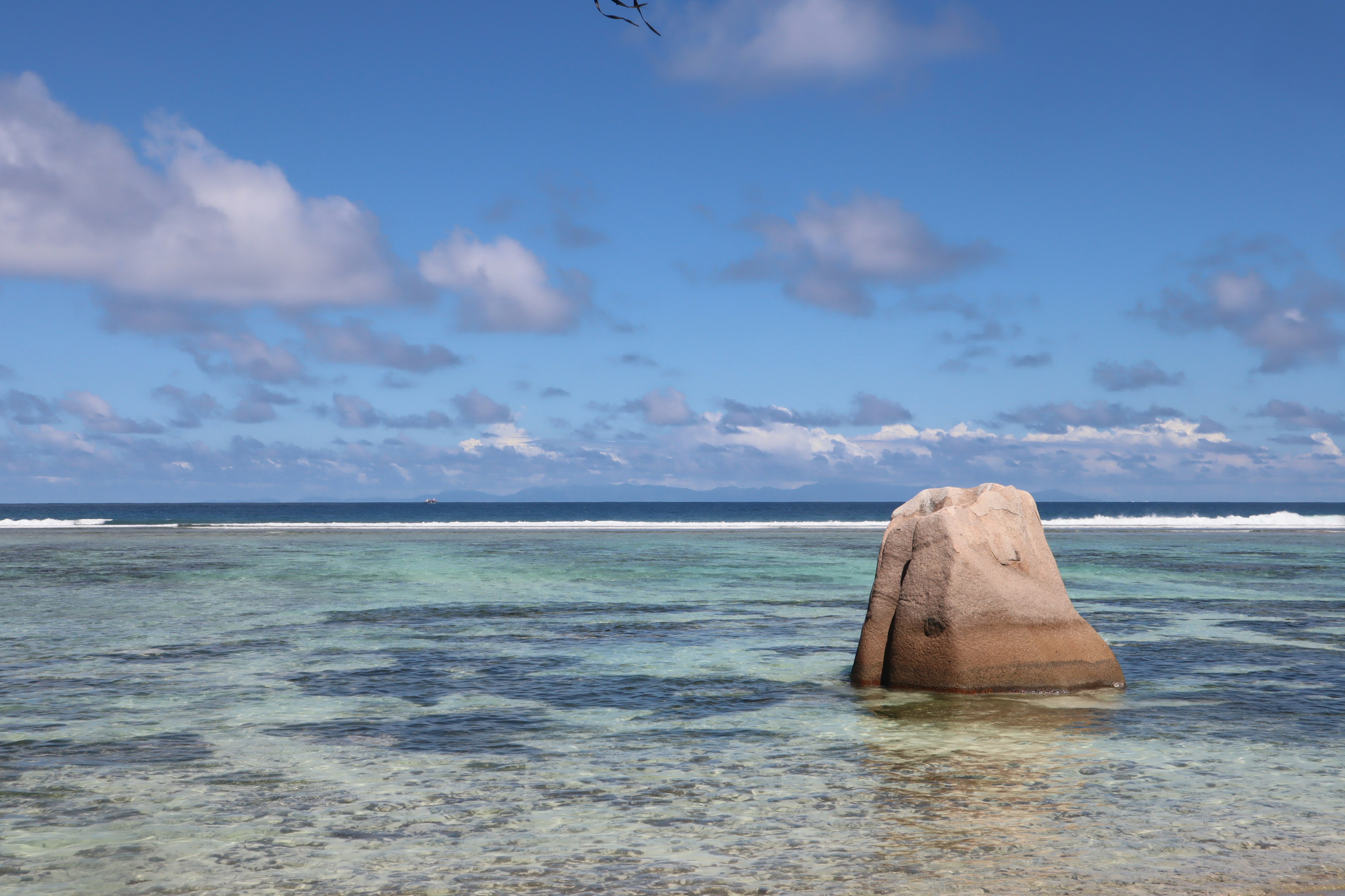 Large rock standing in clear blue water under a bright sky