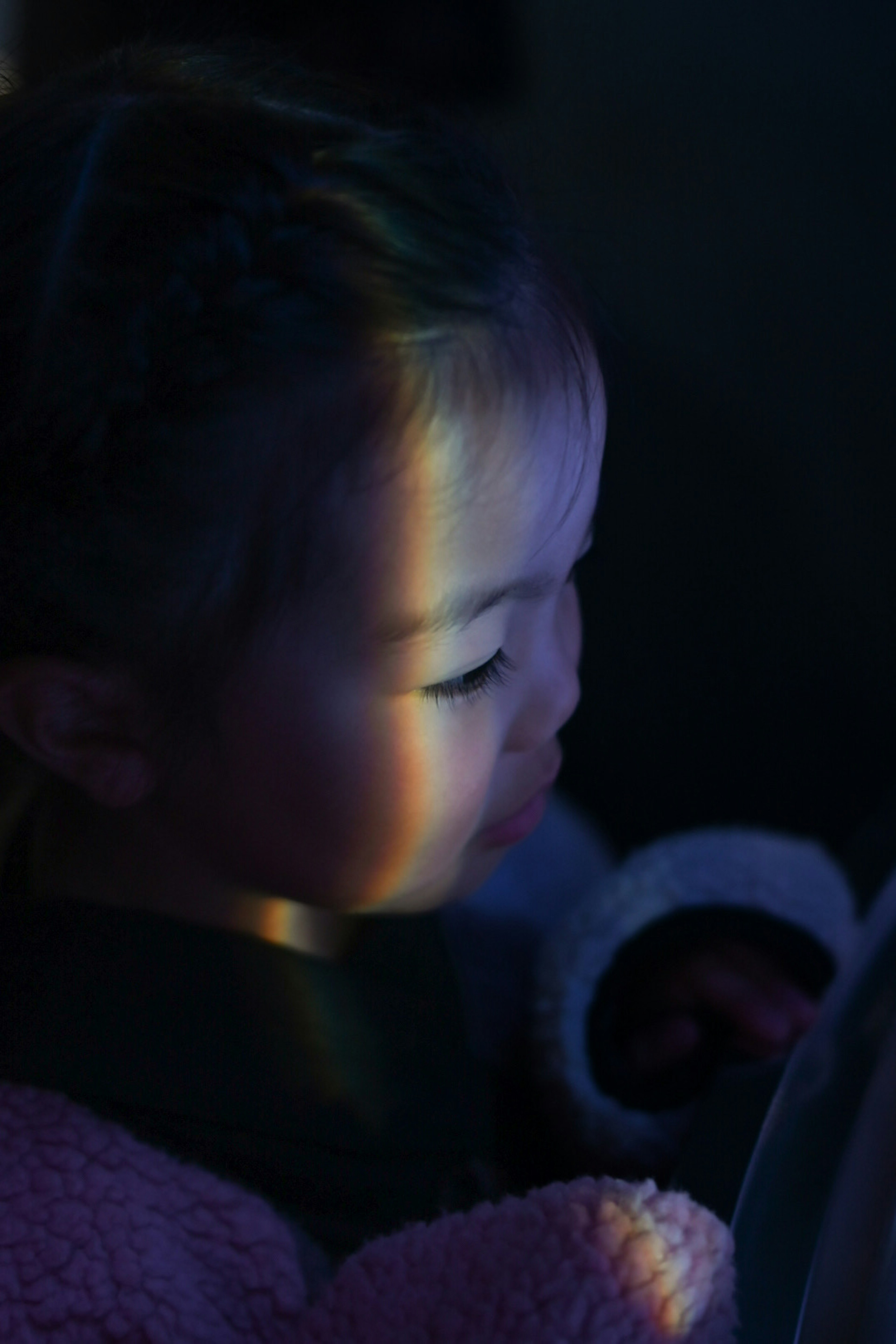 A young girl illuminated by a stripe of light against a dark background