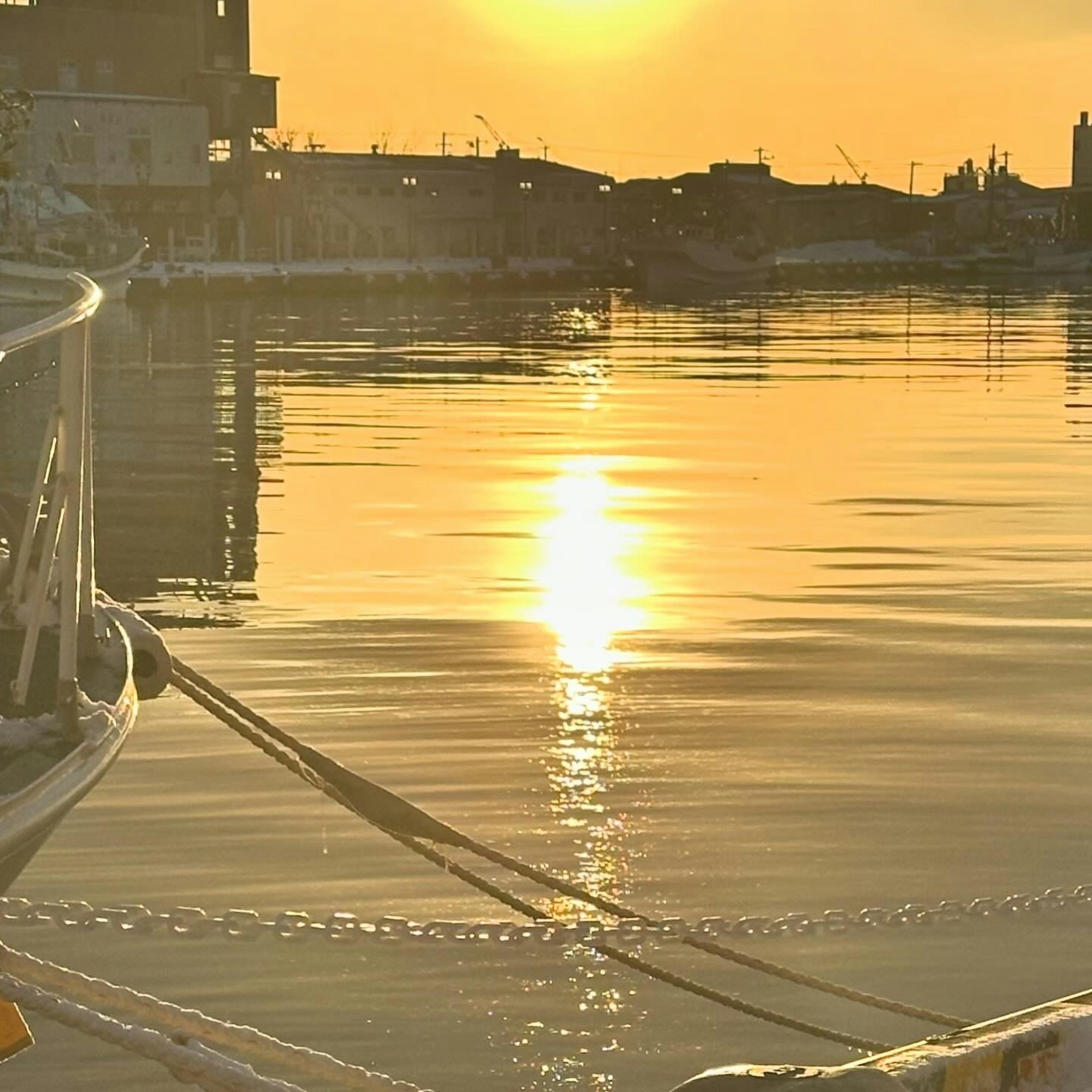 Ruhige Wasseroberfläche, die den Sonnenuntergang und einen Teil eines Bootes spiegelt