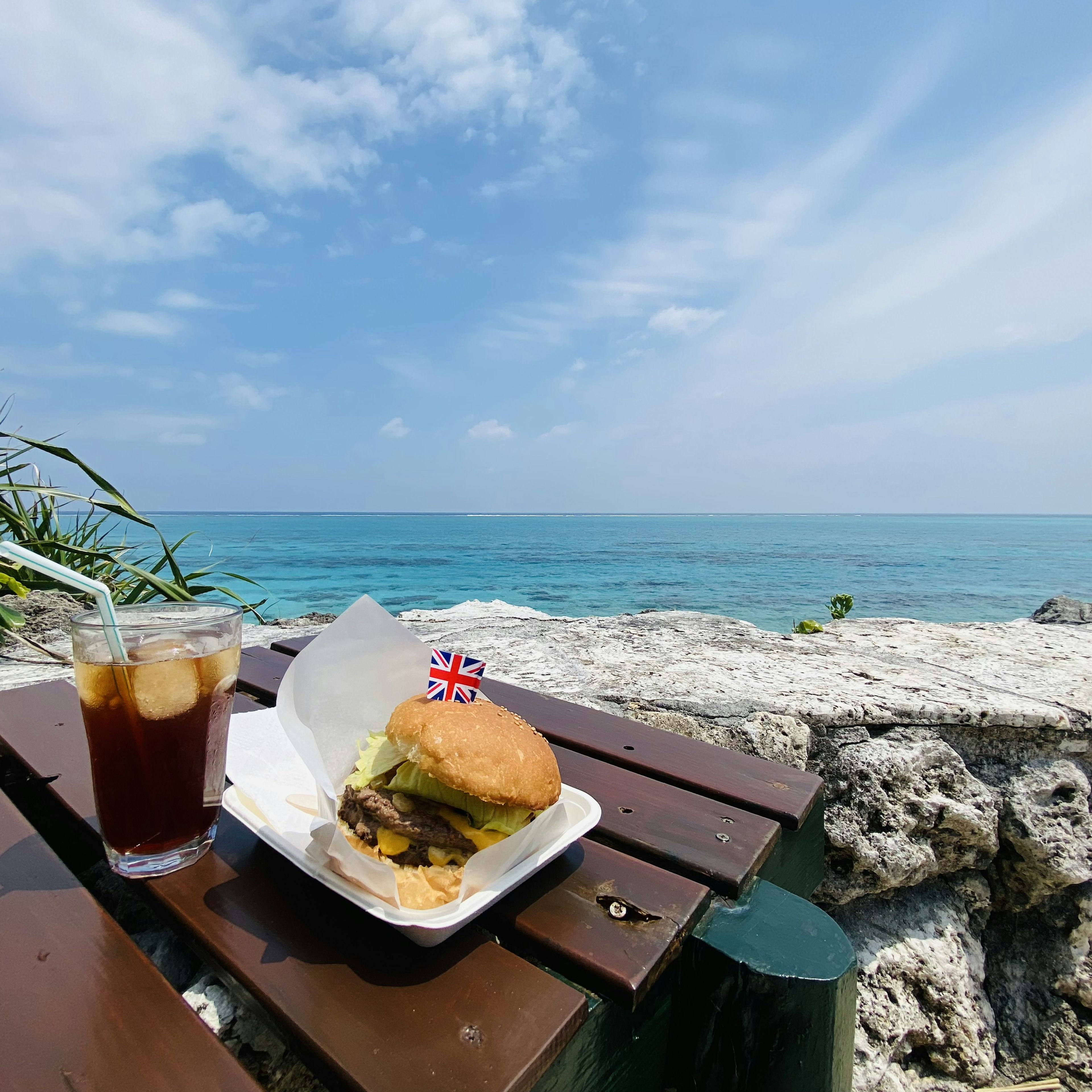 海と青空を背景にしたハンバーガーとアイスティーの画像